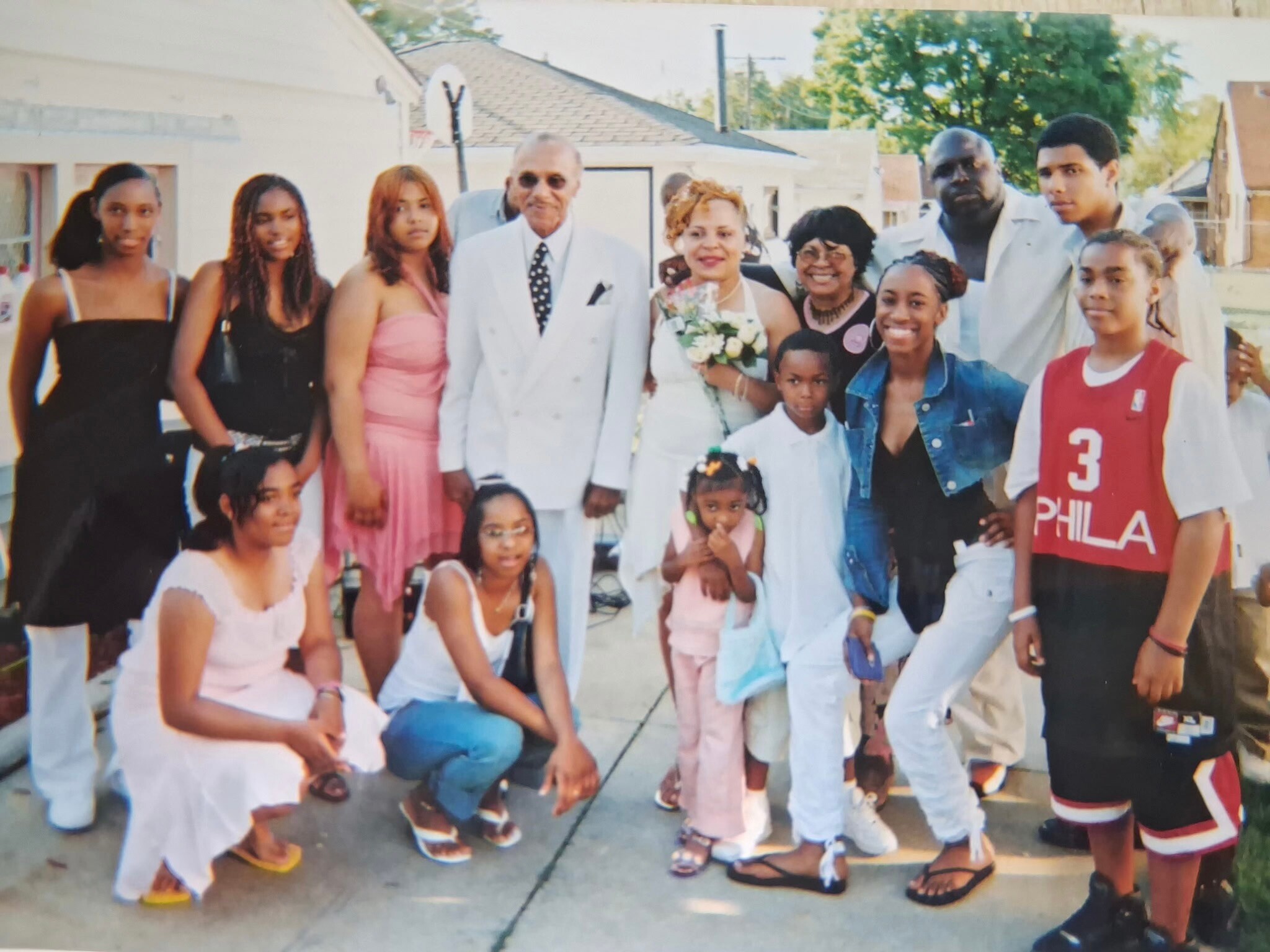Bride and groom stand with family and friends outdoors, posing for a group photo at a celebration.