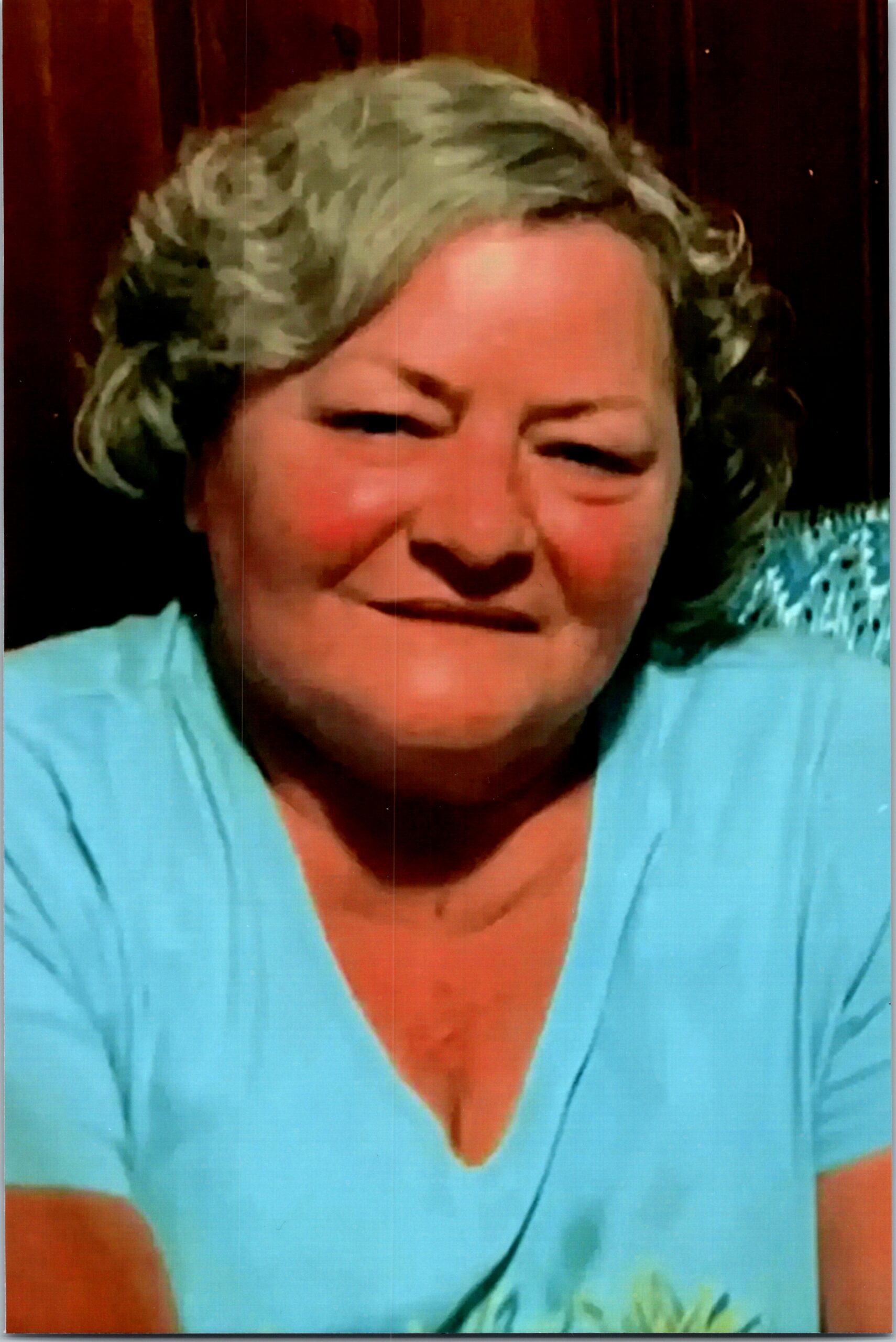 Close-up portrait of a smiling older woman with gray hair wearing a light blue top.