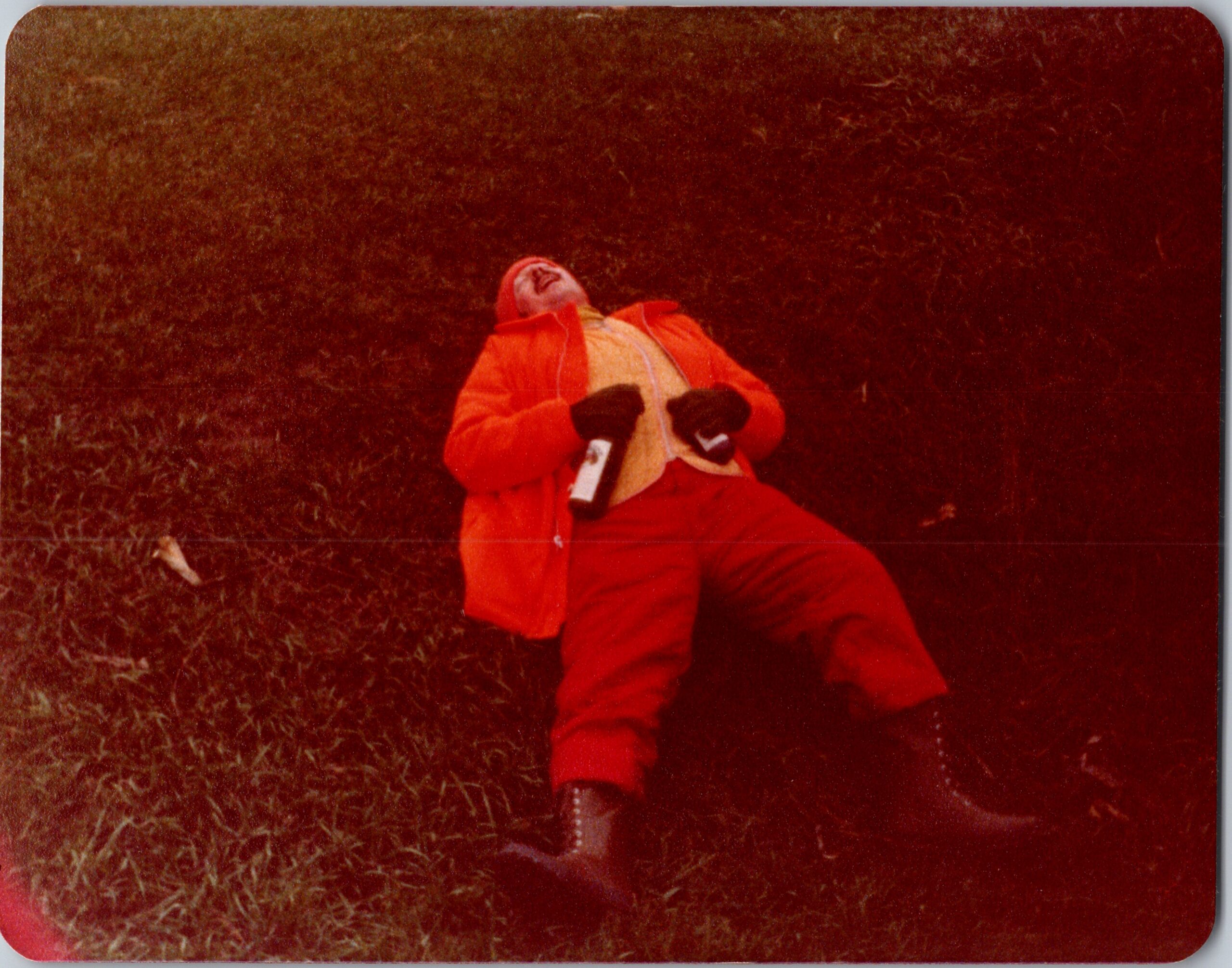Person in bright red winter suit lying on grass, head tilted back in laughter.
