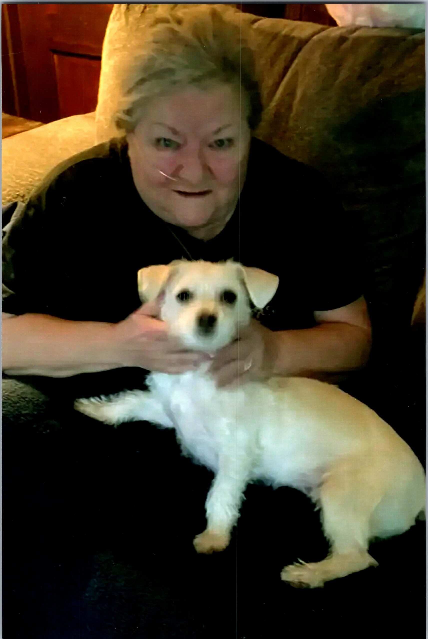 Older person seated on a couch with a small white dog resting on their lap, looking at the camera (home setting).