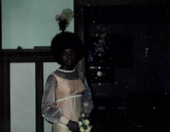 Young woman in a vintage cream dress with sheer sleeves, holding a bouquet indoors near a doorway.