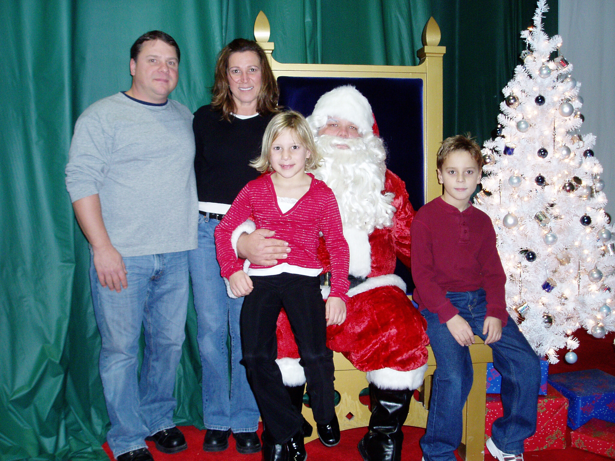 Family group posing with Santa Claus beside a white, ornamented Christmas tree indoors.
