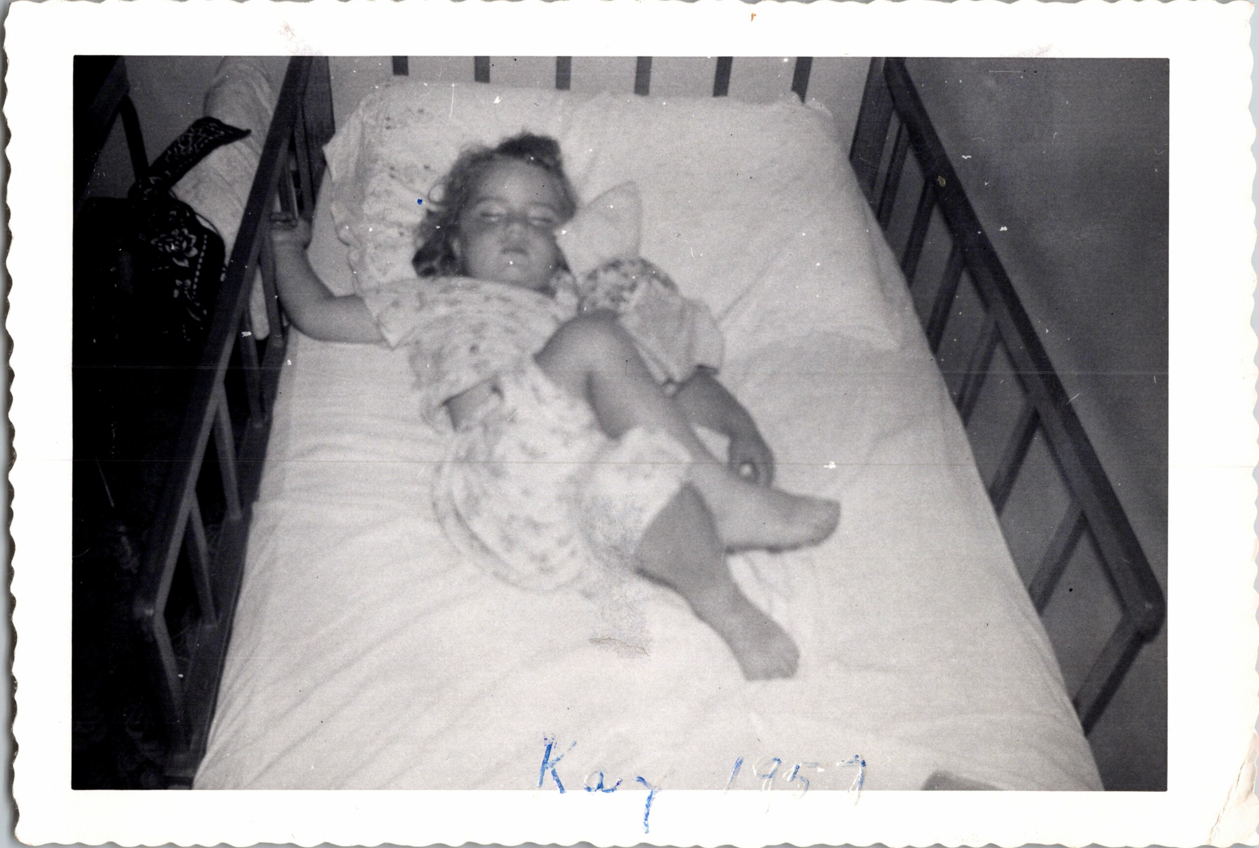 Child sleeping in a bed, tucked in with a light blanket and pillow, looking toward the camera.