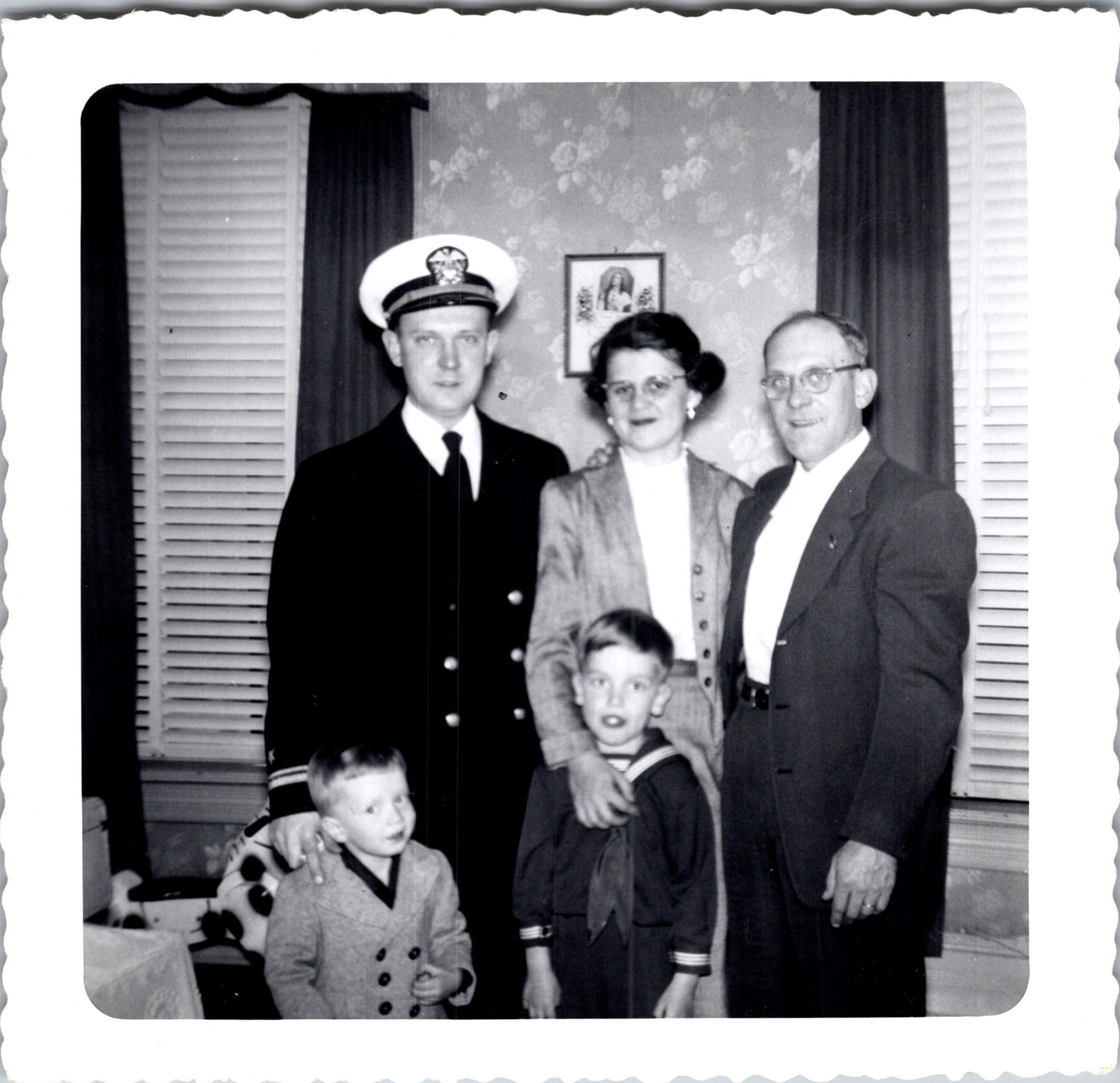 Family portrait with a naval officer, a woman, and two men flanked by two children indoors.