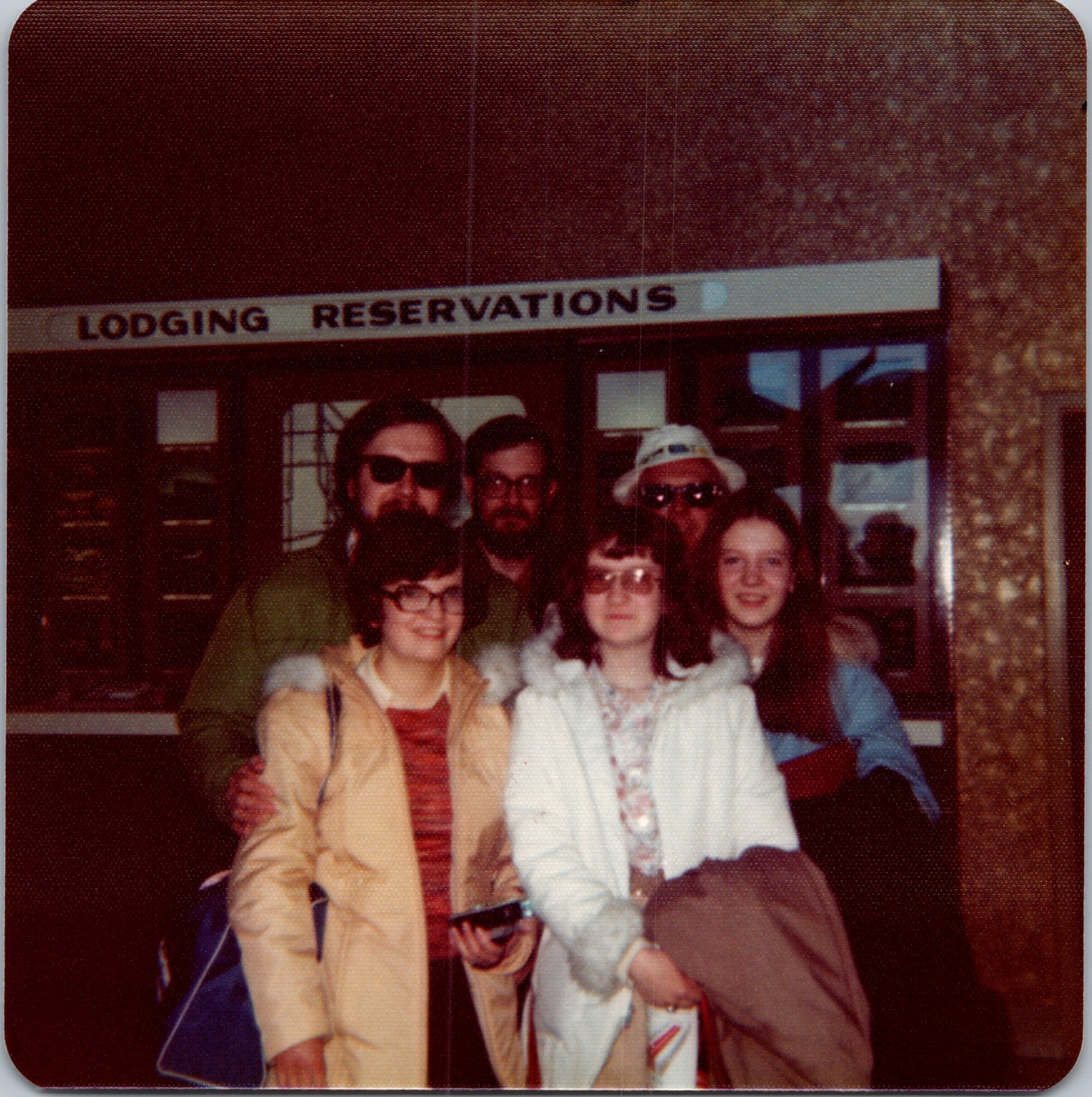 Group of people posing for a photo outside a lodging facility, with a 'Lodging Reservations' sign above them.