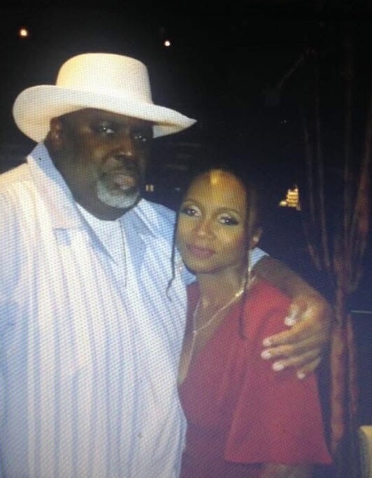 Man wearing a white hat and striped shirt with his arm around a woman in a red top at night, posing for a photo outdoors.