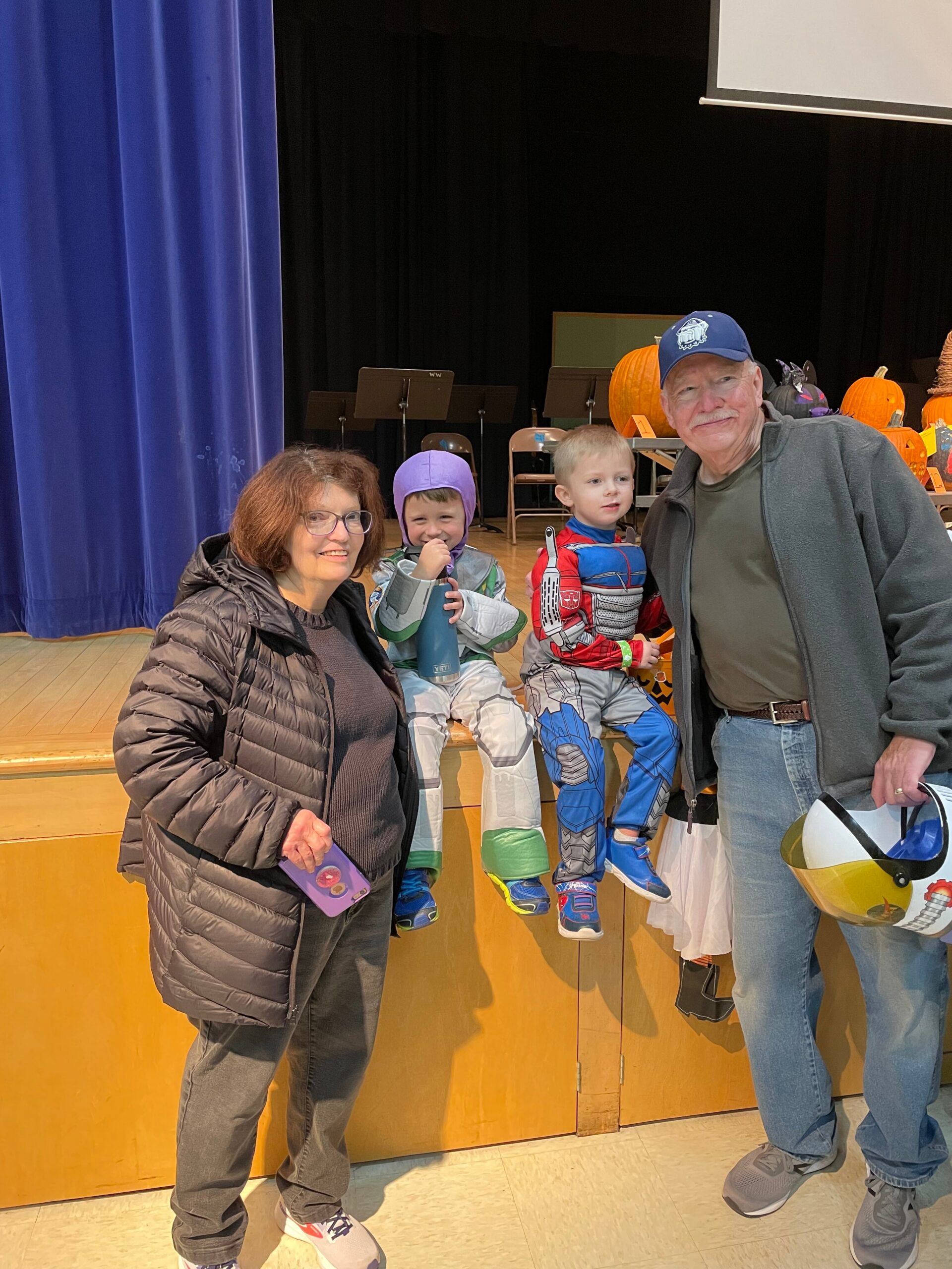 Woman and man stand with two children in costumes on a stage, pumpkins lining the back wall.