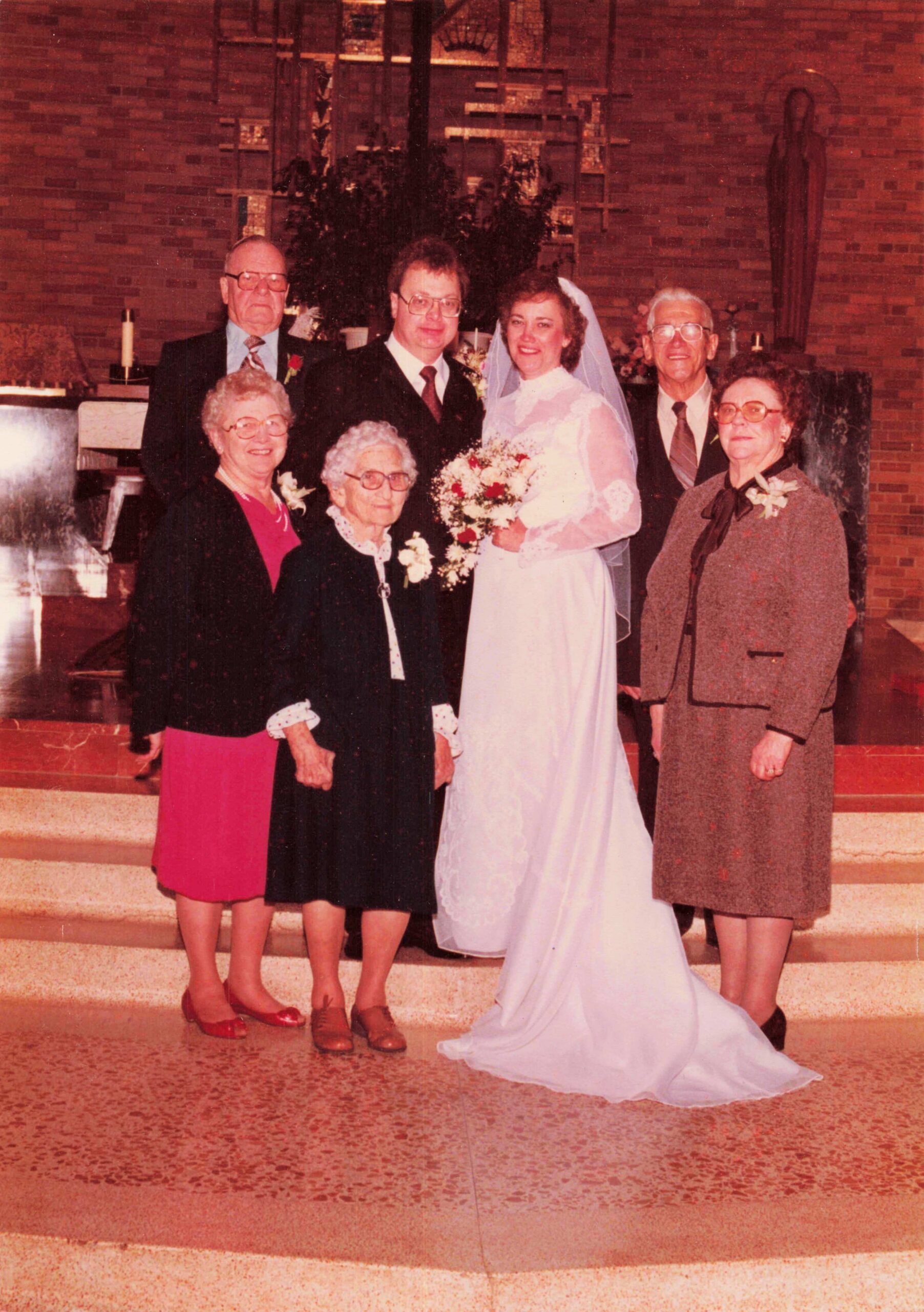Bride in white gown and veil with bouquet posing with family at a wedding inside a church.