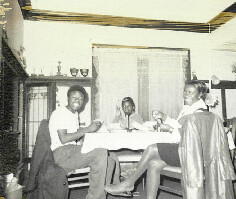 Four people sit around a dining table in a home, looking at papers and chatting.