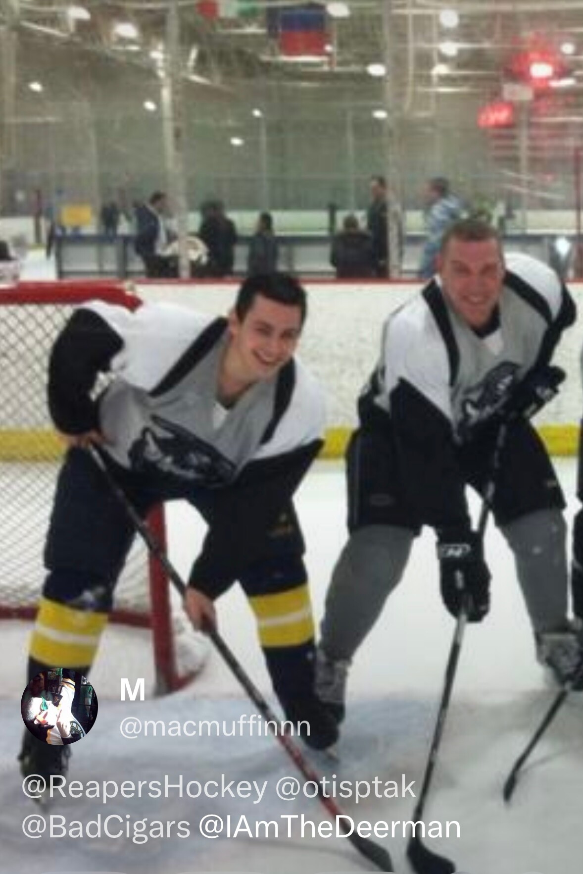 Two hockey players in white jerseys bend over and smile on the ice near the goal on an indoor rink.