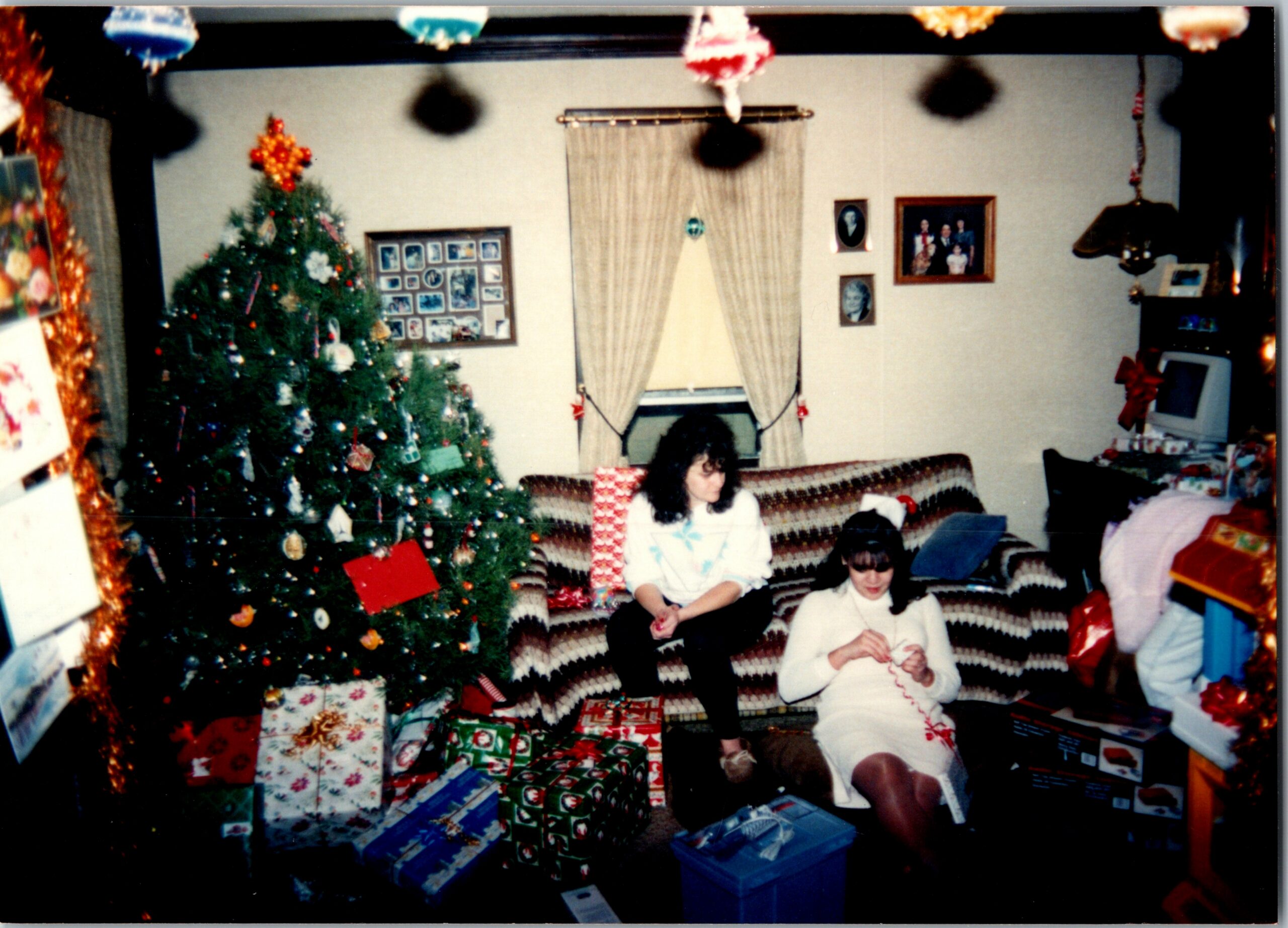 Living room Christmas scene with a tall tree and many wrapped presents; children sit on the floor opening gifts.