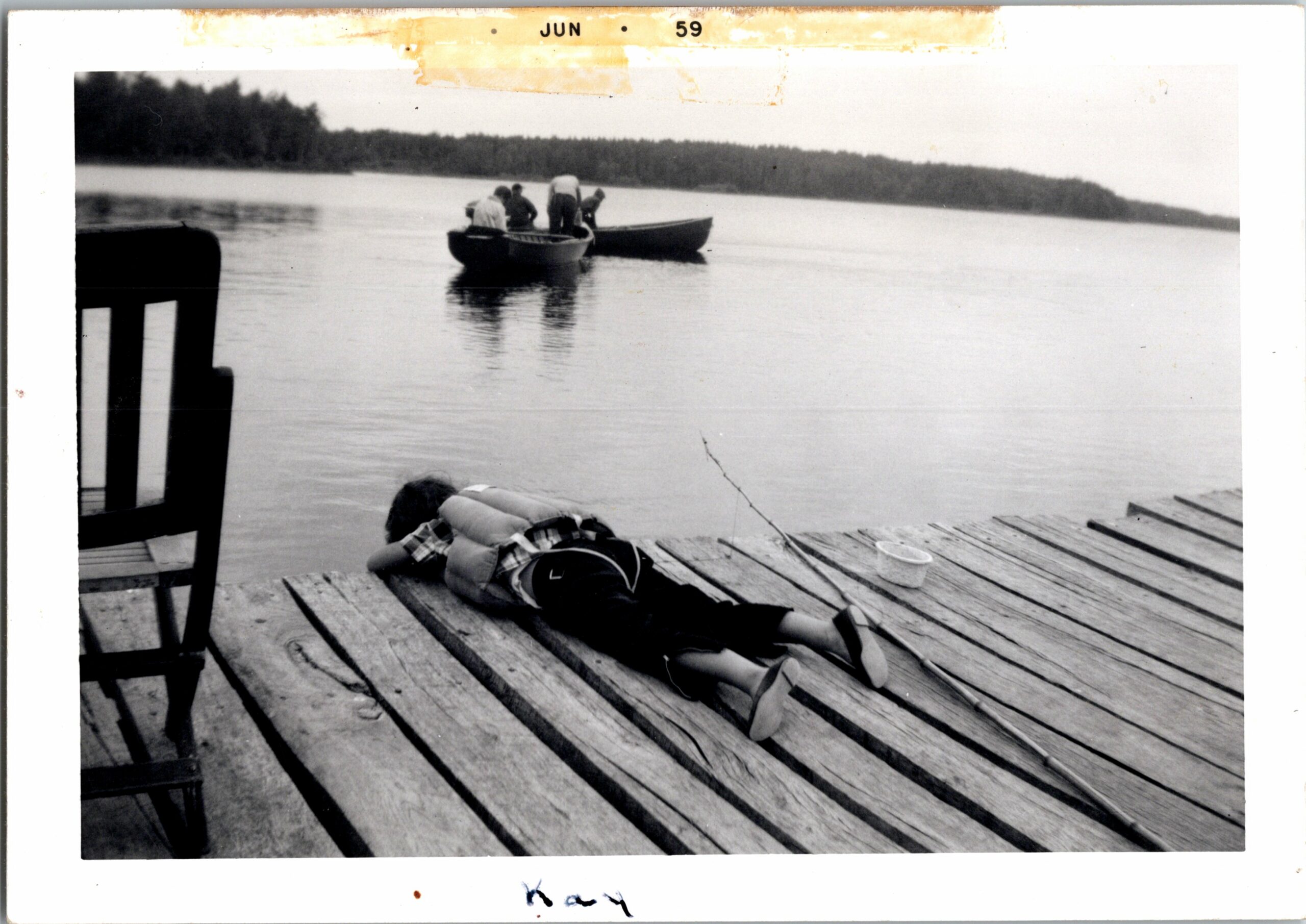 People in a small boat on a calm lake near a wooden dock; several life jackets lie on the dock.