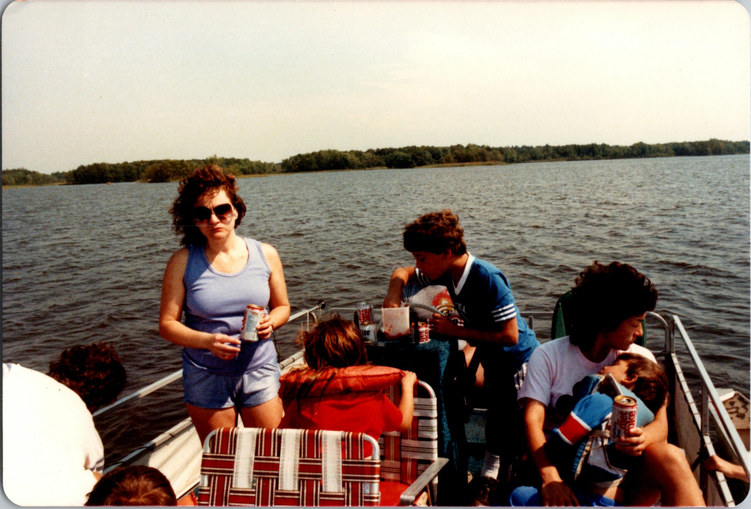 Group of people on a boat at the lake, some holding drinks, enjoying a sunny day.