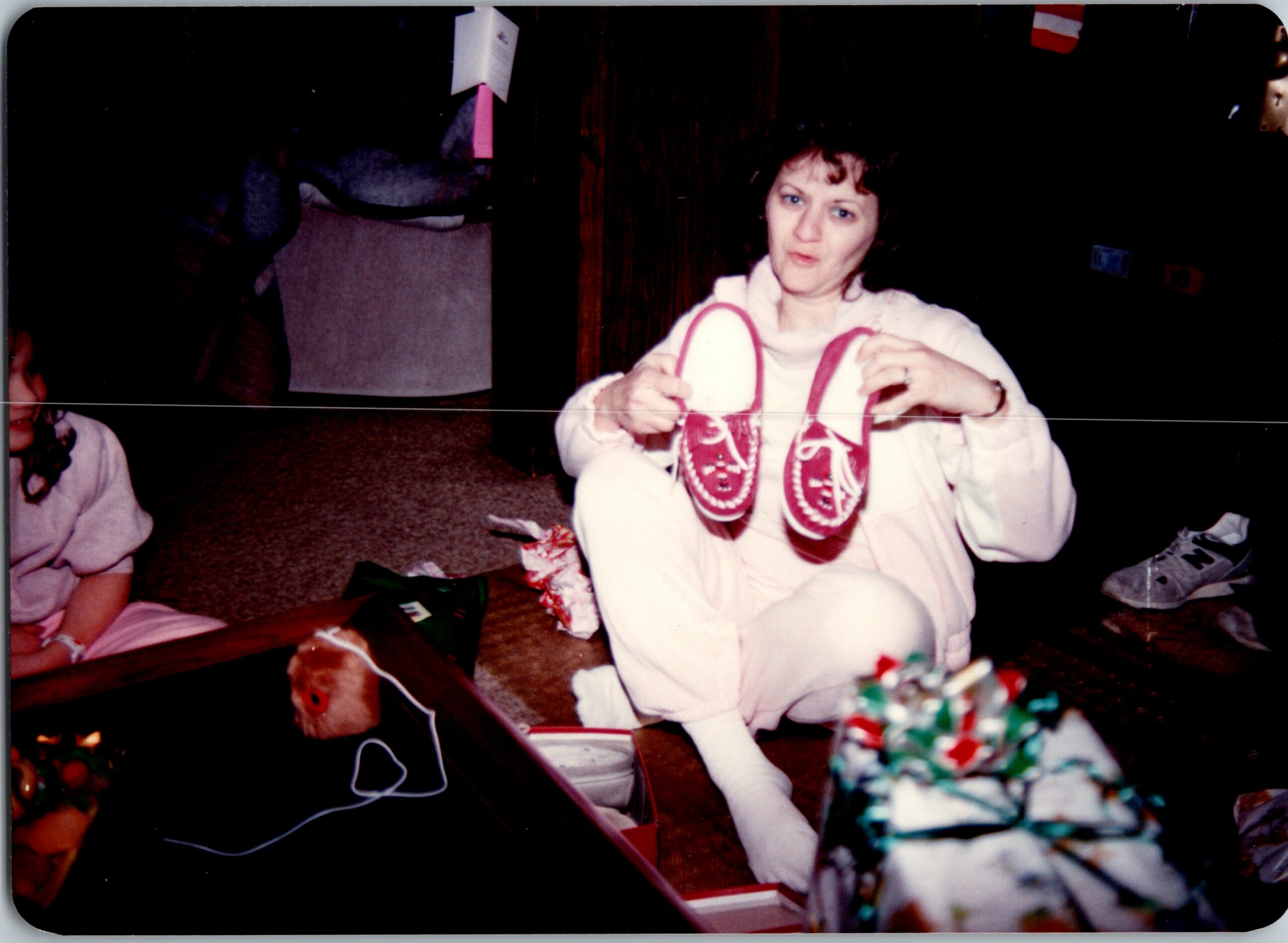 Woman in a white robe shows a pair of red sneakers during a Christmas gift scene at home.