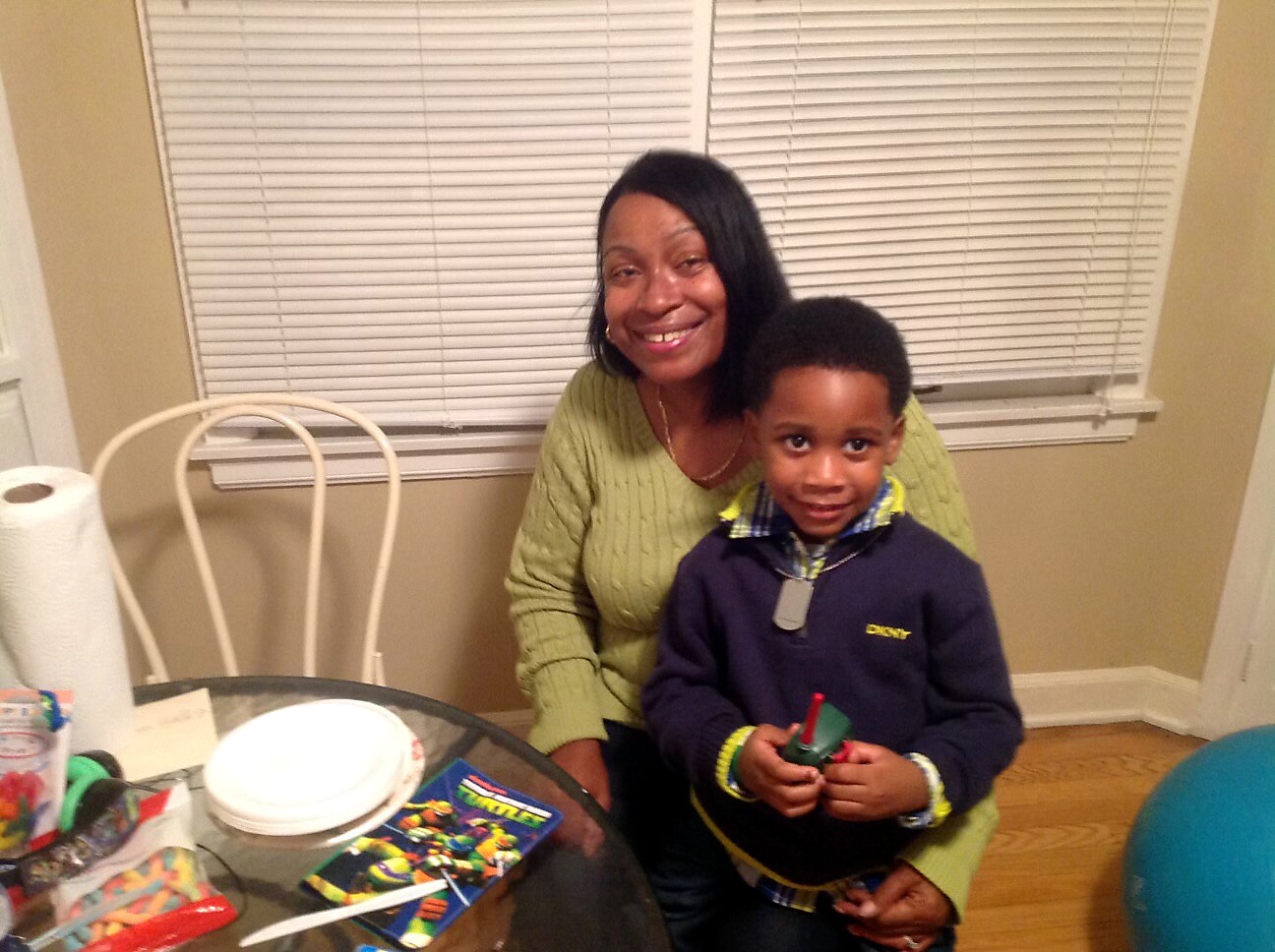 Smiling woman in a green sweater seated with a young boy at a table indoors, posing for a photo.