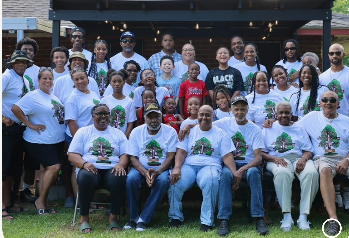 Diverse group of people wearing white T-shirts with a tree graphic posing for a group photo on a backyard lawn.