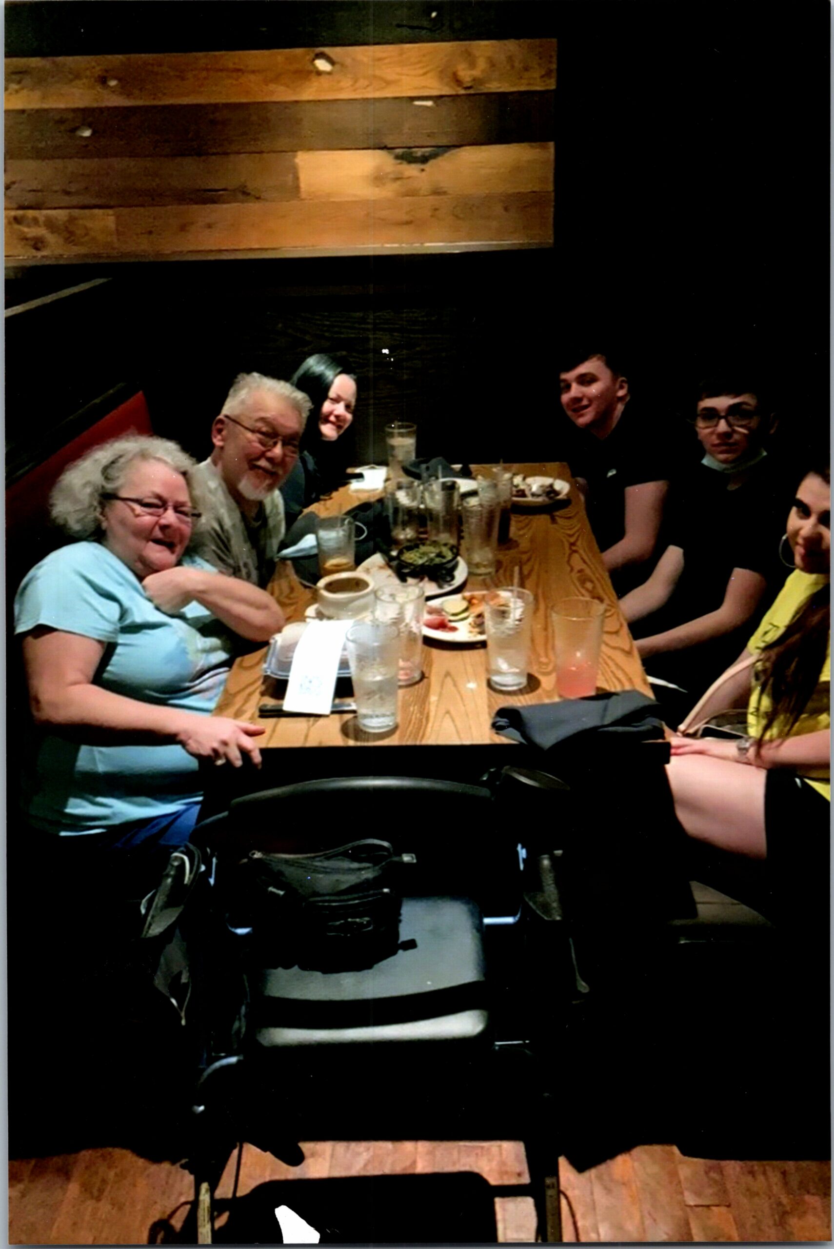 Group of six people seated around a wooden restaurant table, smiling and chatting at a dinner gathering.