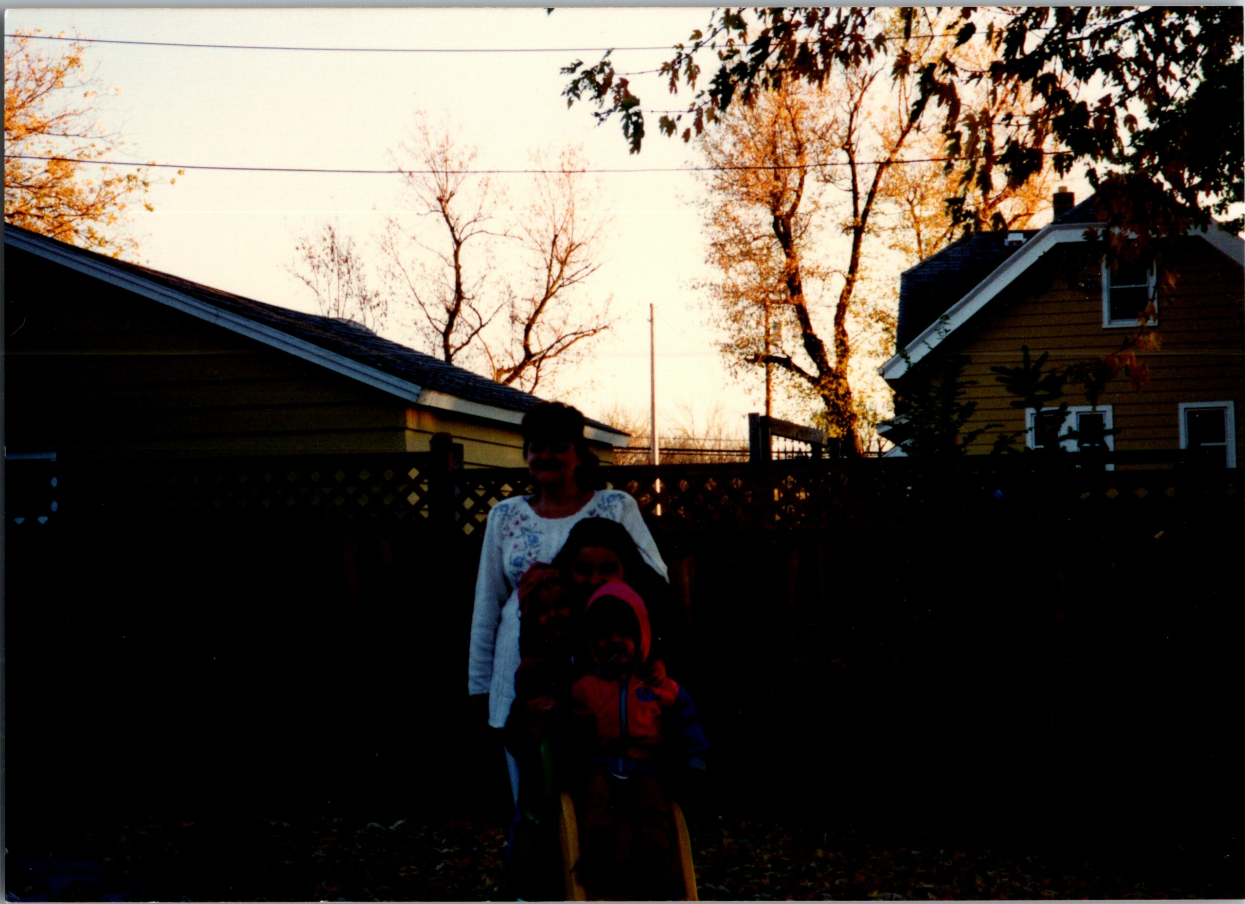 Autumn backyard scene between two houses with leafless trees and clotheslines; three children stand in shadows near a fence.
