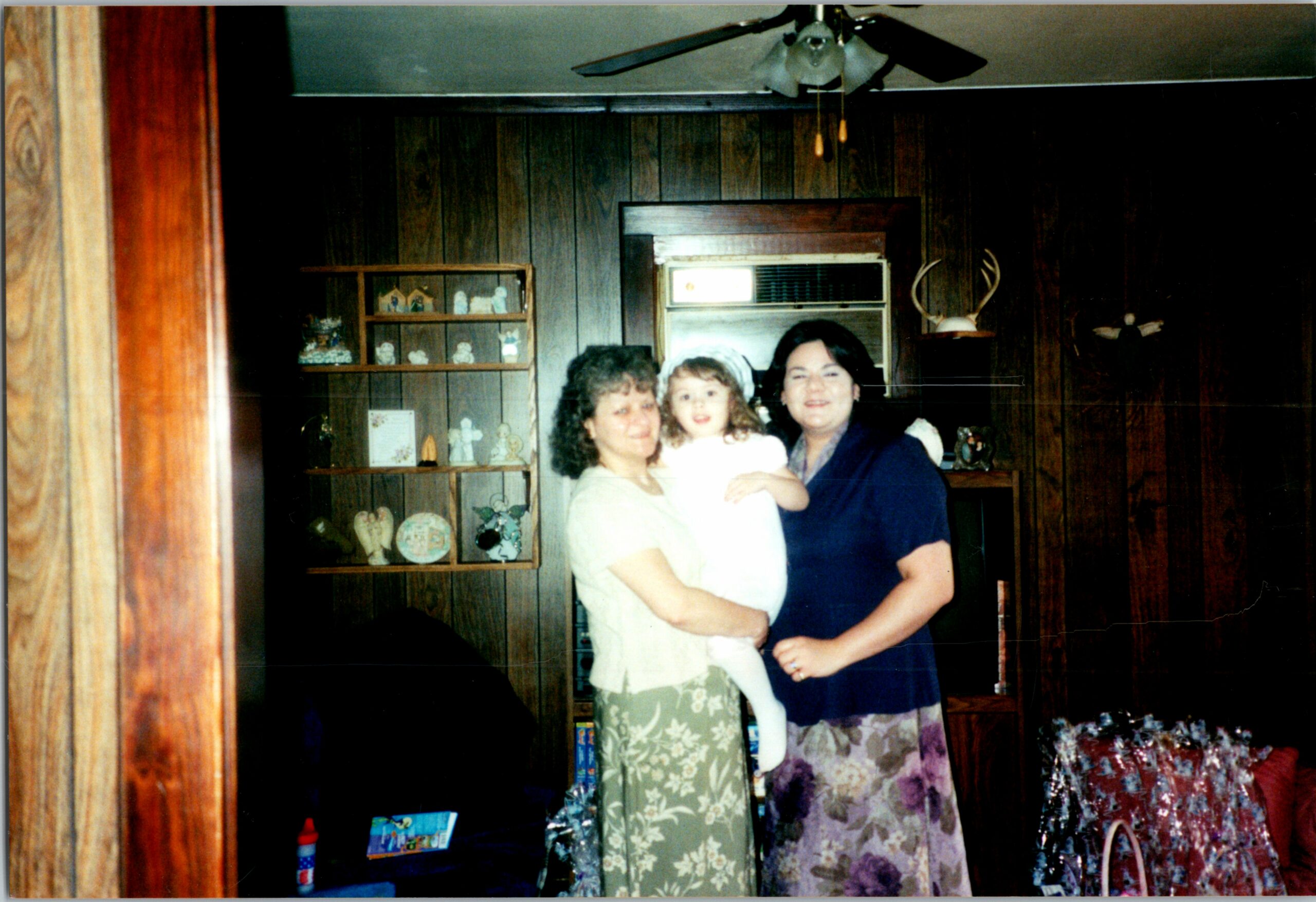 Three women posed together indoors in a wood-paneled room, smiling at the camera.
