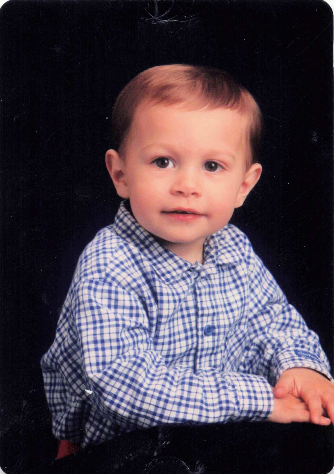 Young child in a blue-and-white checkered shirt posed against a black background for a portrait.