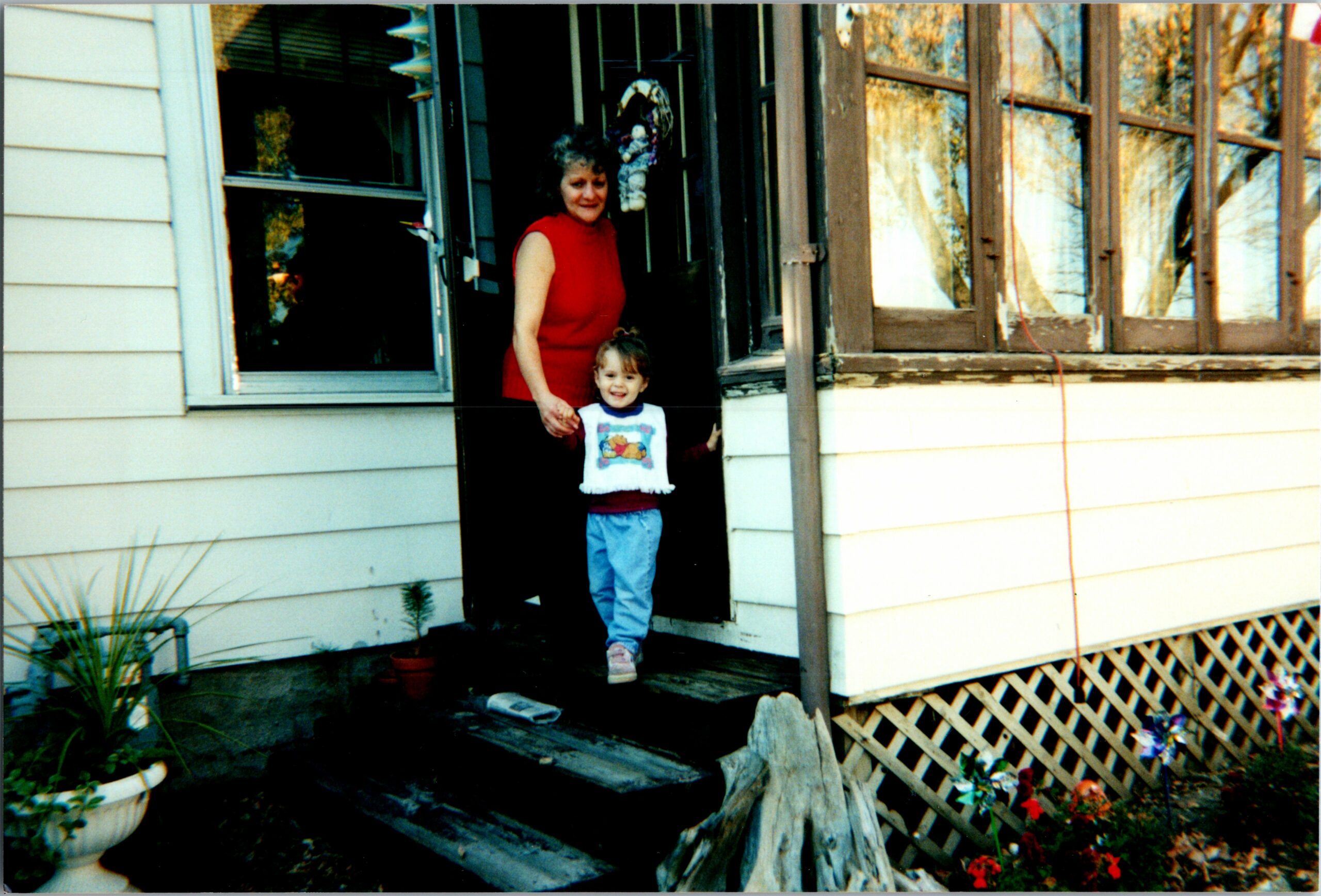 Woman in a red sleeveless top stands in a doorway, holding hands with a smiling young girl at the home’s entrance.
