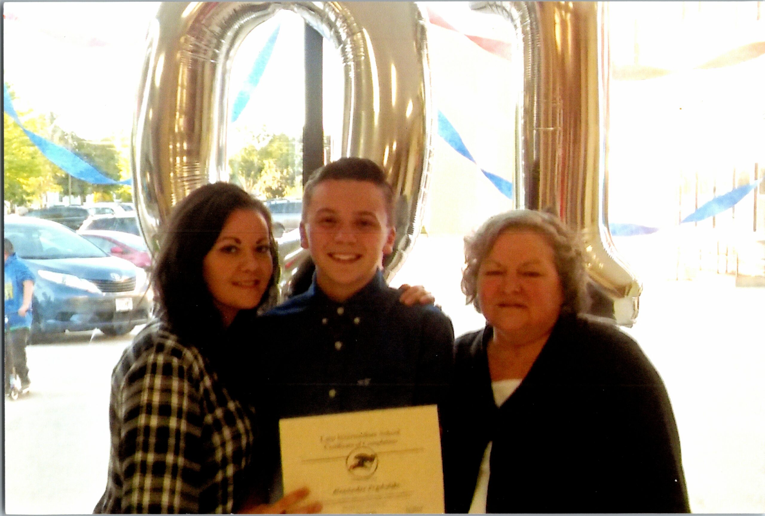 Three people pose for a photo, holding a certificate with a large metallic 80 balloon behind them.