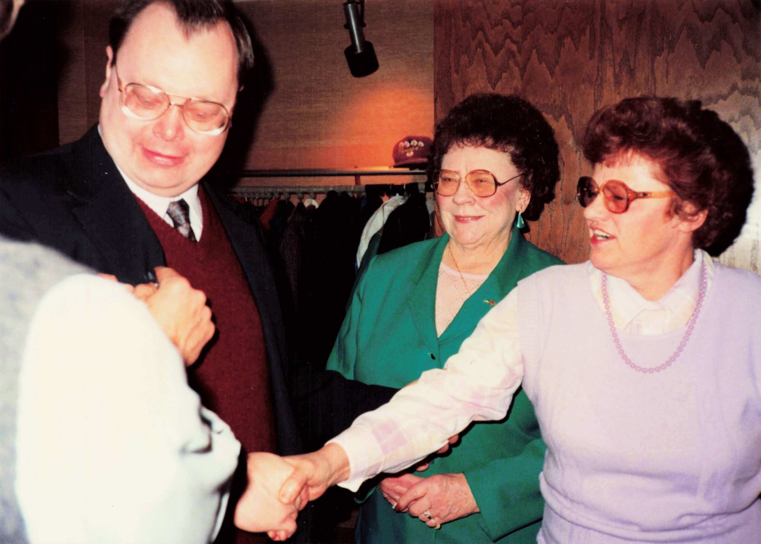 Three older adults holding hands and dancing together, smiling at a social gathering.