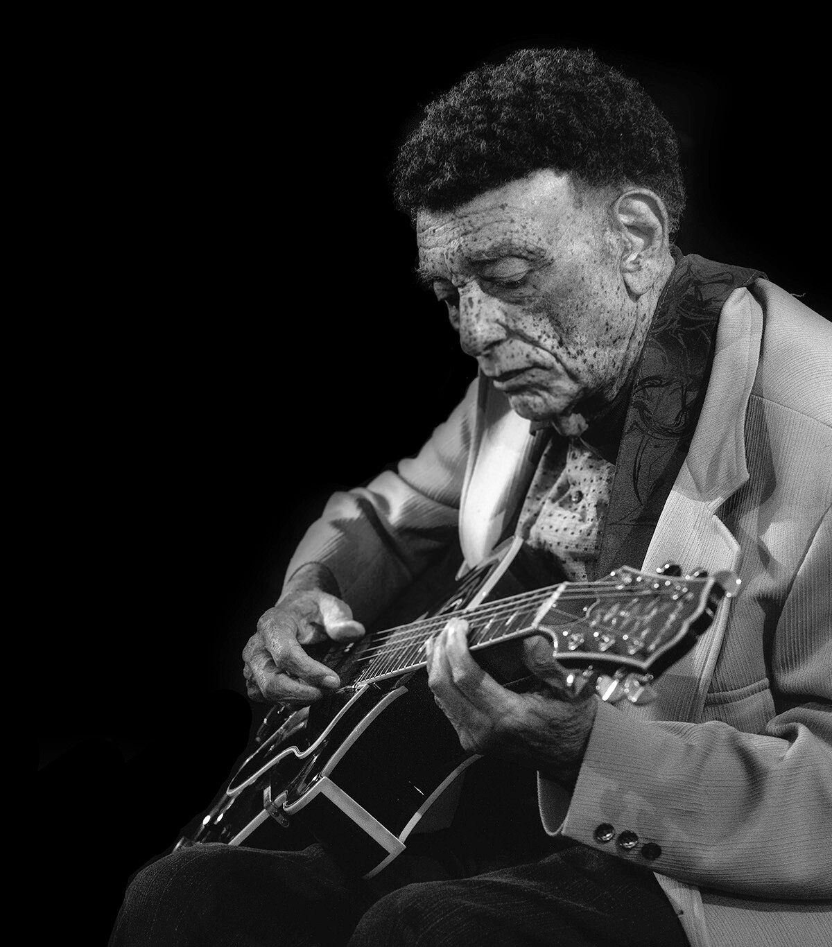 Black-and-white portrait of a man intensely playing an acoustic guitar, gazing down at the neck.