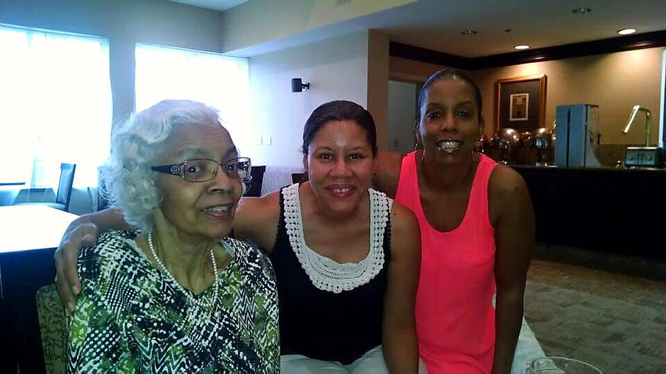 Three women sit close together and smile at the camera in a lounge area.