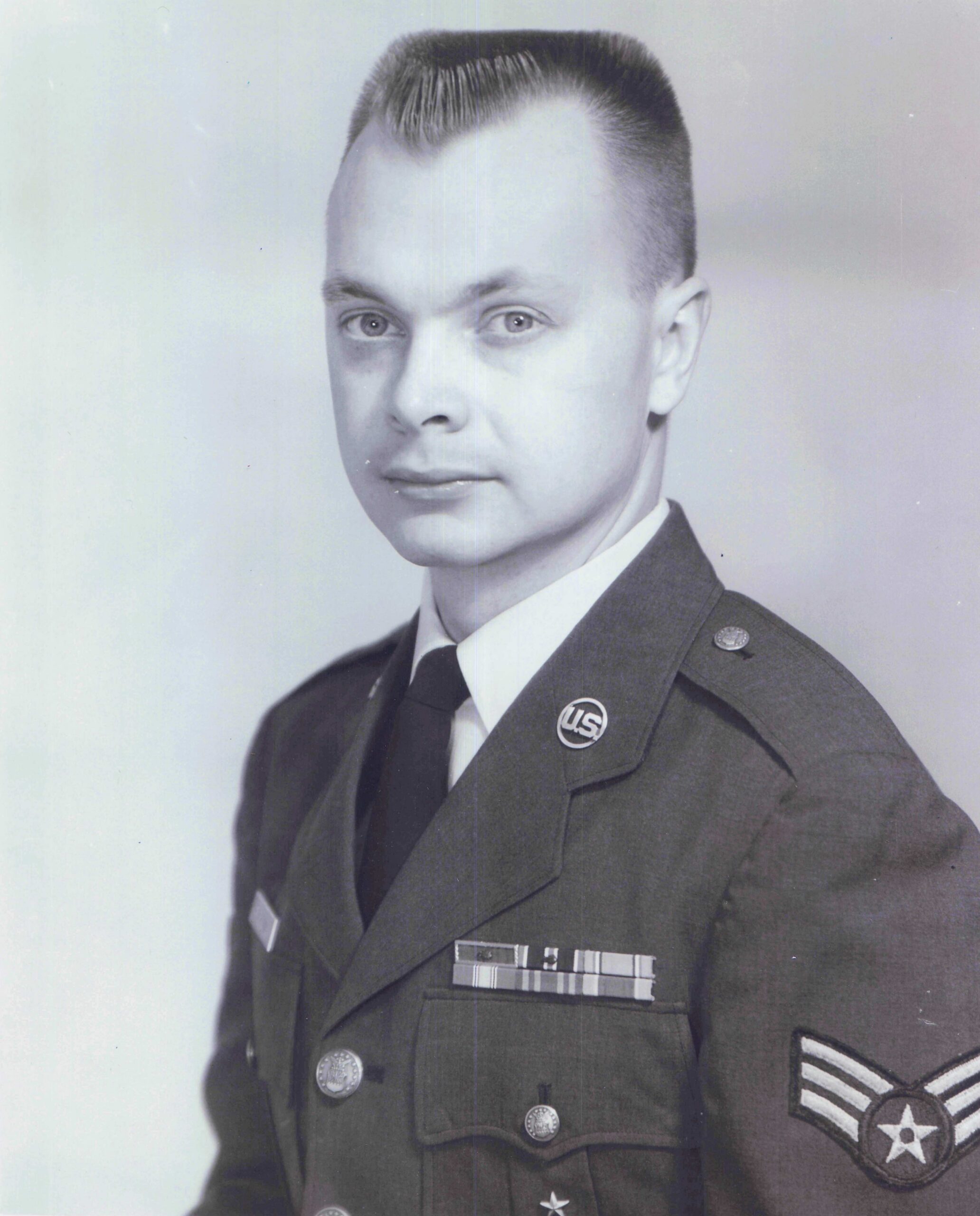 Black-and-white portrait of a man in a military dress uniform, with ribbons and insignia on the chest and a sergeant-style patch on the sleeve.