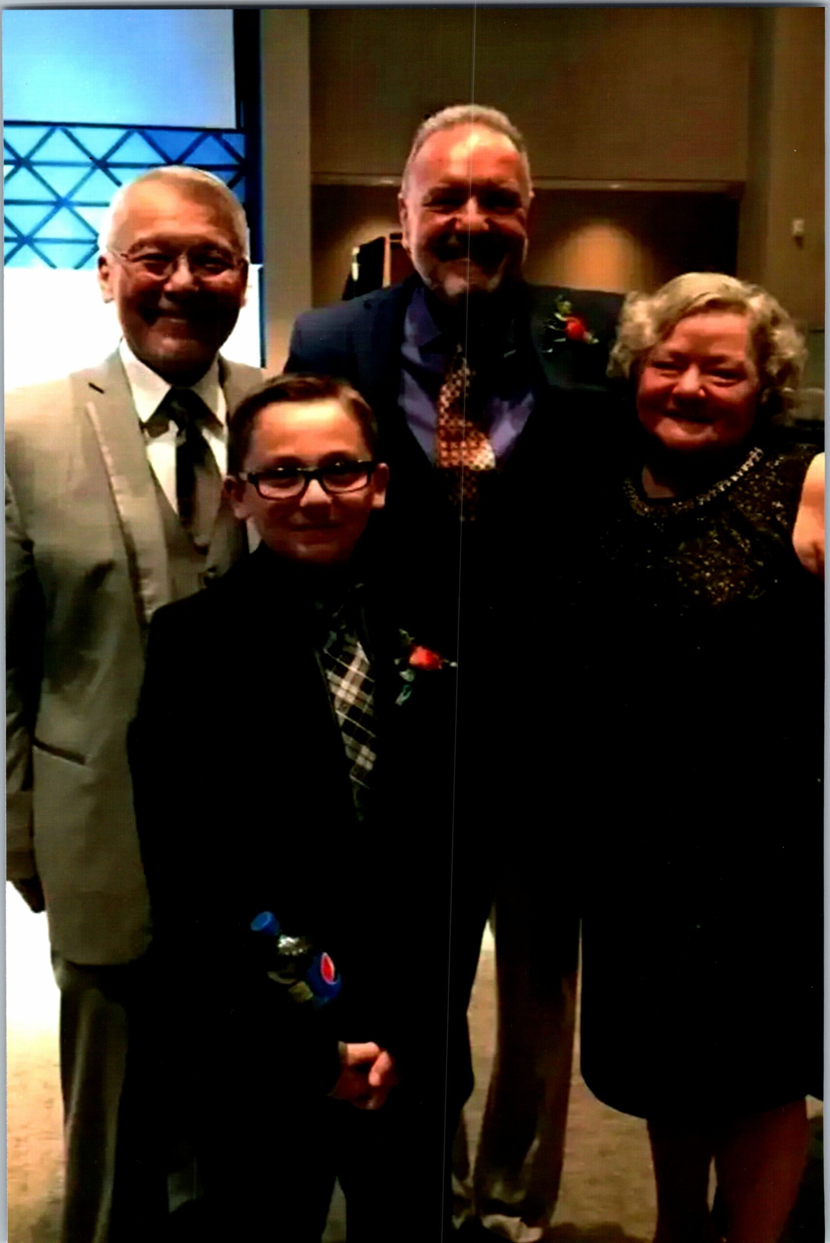 Four adults in formal attire posing together and smiling at a photoshoot during an event.