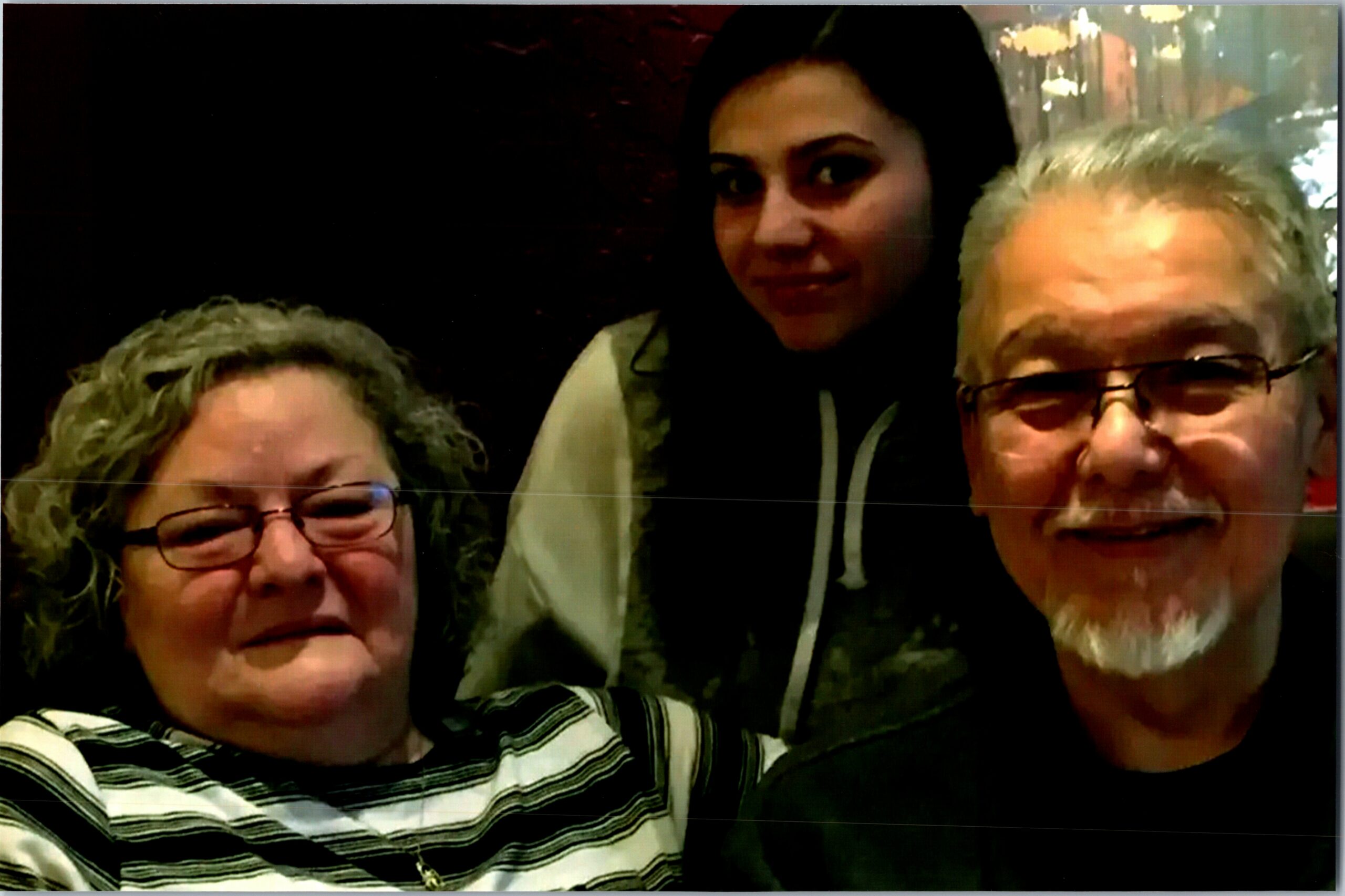 Three friends posing for a close‑up selfie: left woman with glasses, center woman wearing a hijab, right man with glasses, all smiling.