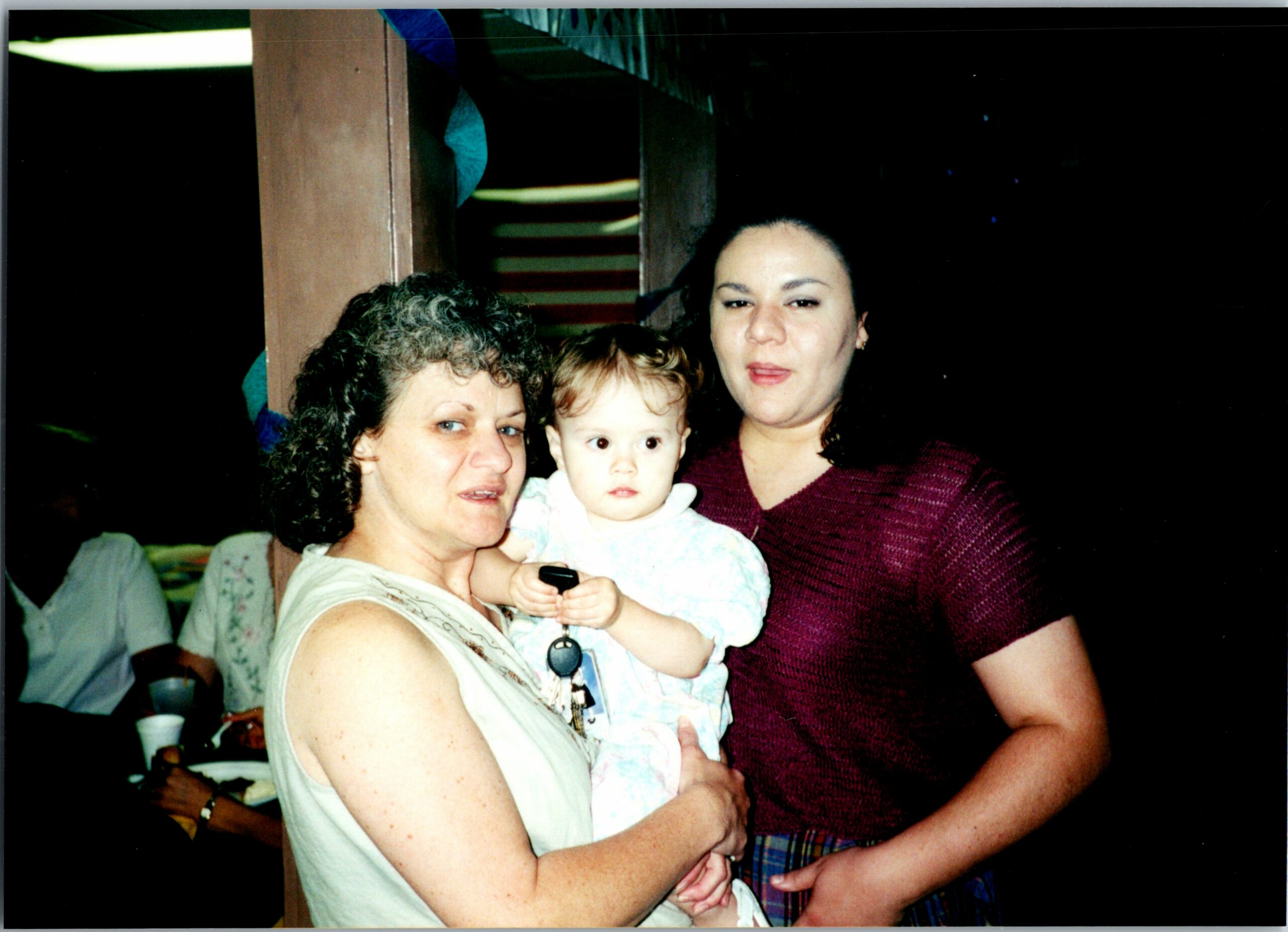 Older woman holding a baby with a younger woman beside them at a family gathering.