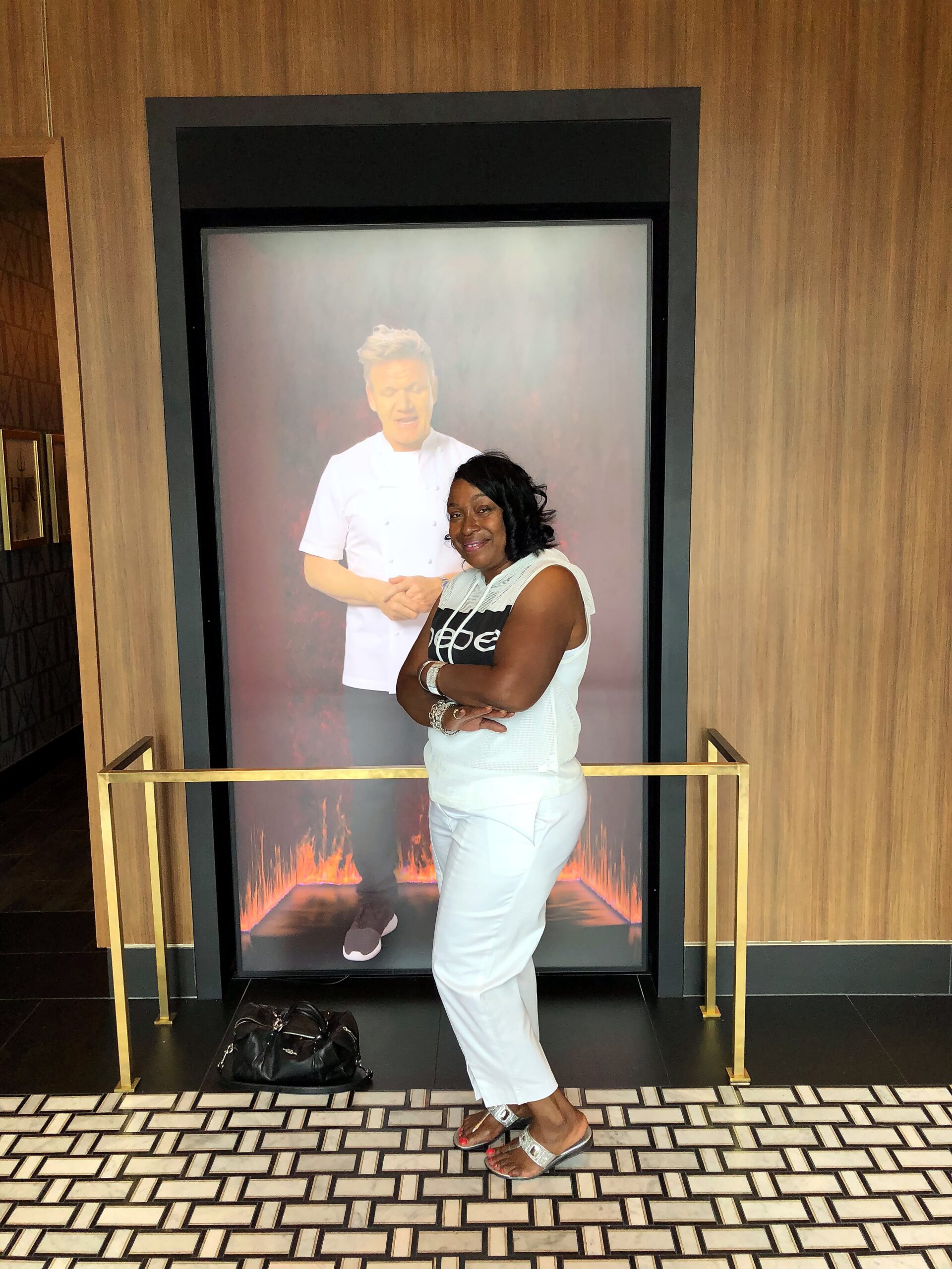 Woman in white outfit posing in front of a large poster of a chef with a fiery background.