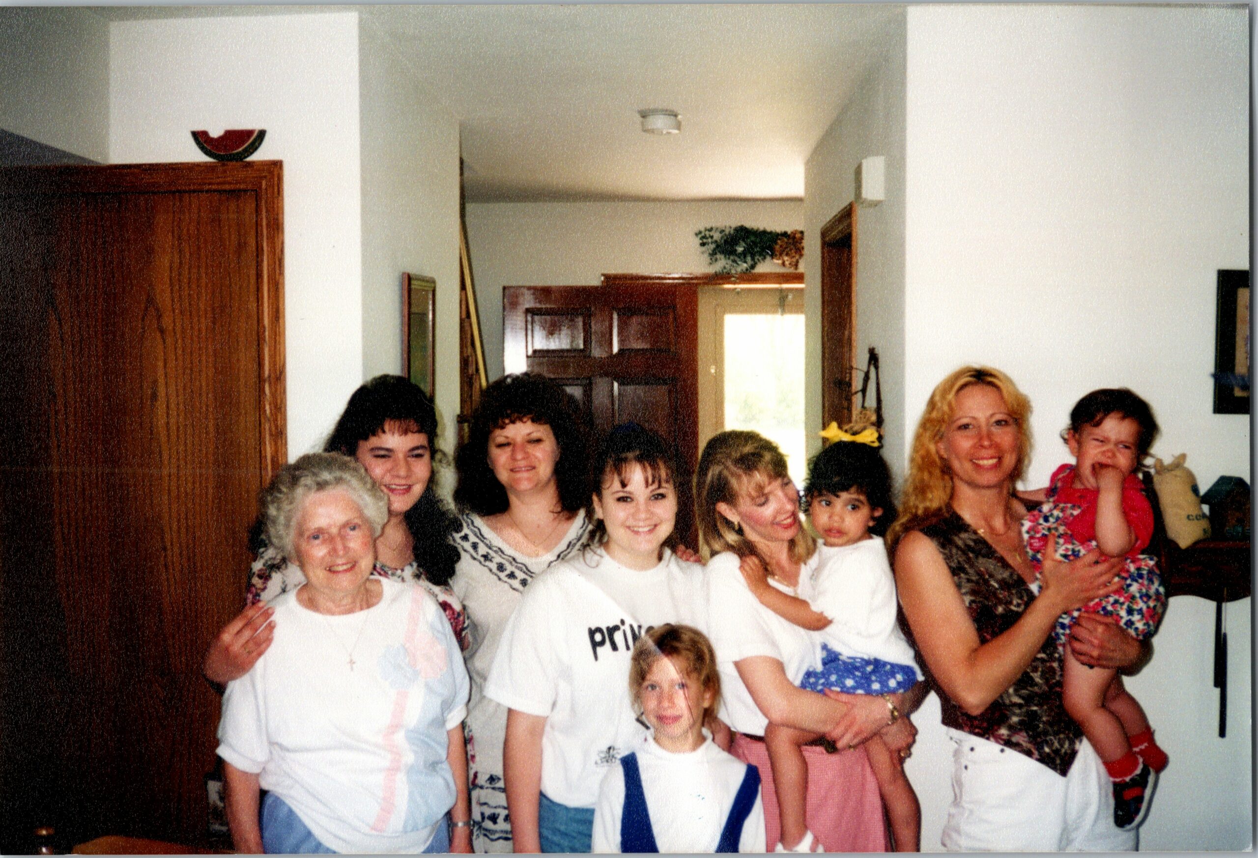 Group of smiling women and children posing together in a living room, likely a family gathering or party indoors.