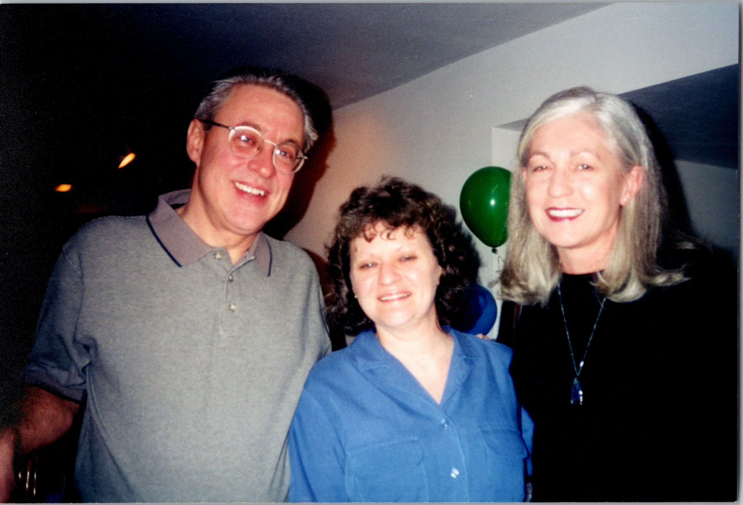 Group of four adults smiling for a photo at a party, with a green balloon in the background.