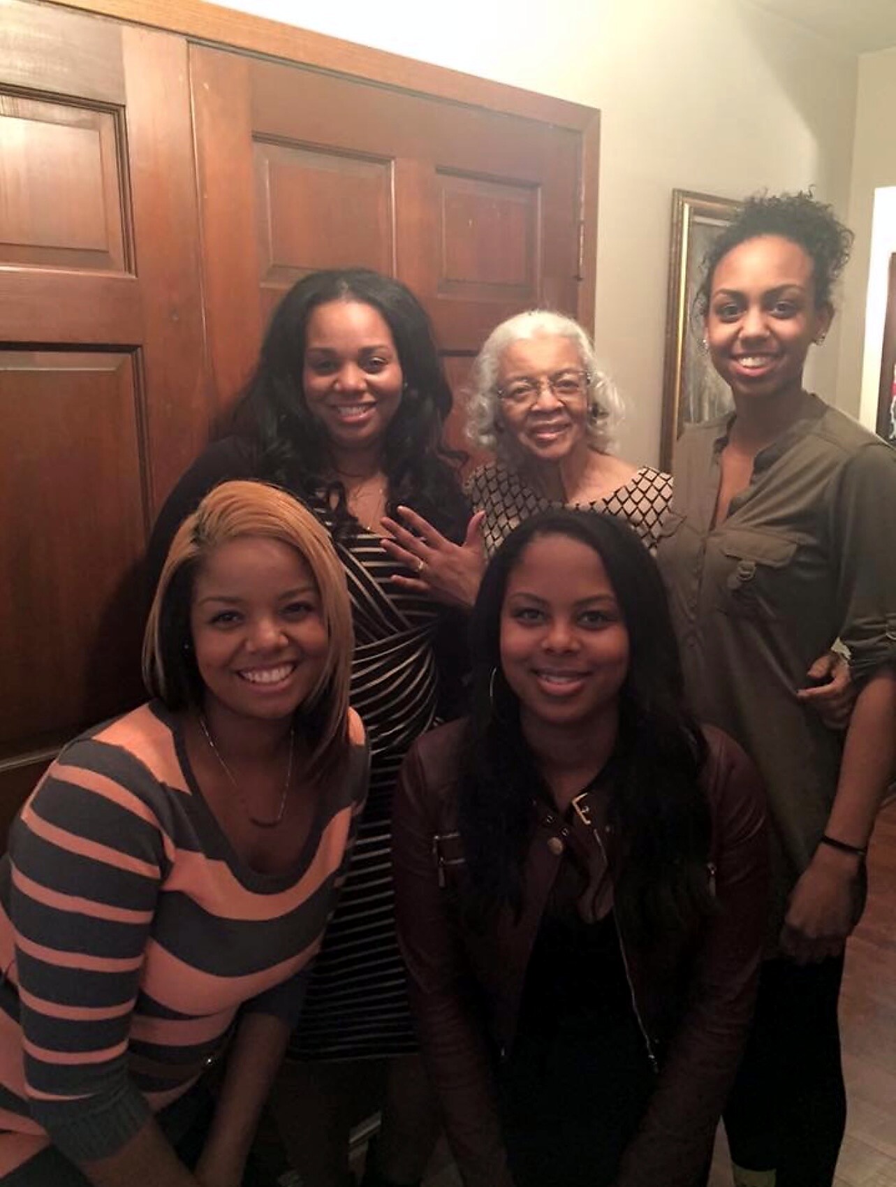 Group of five women posing together indoors, standing in front of wooden doors and smiling at the camera.