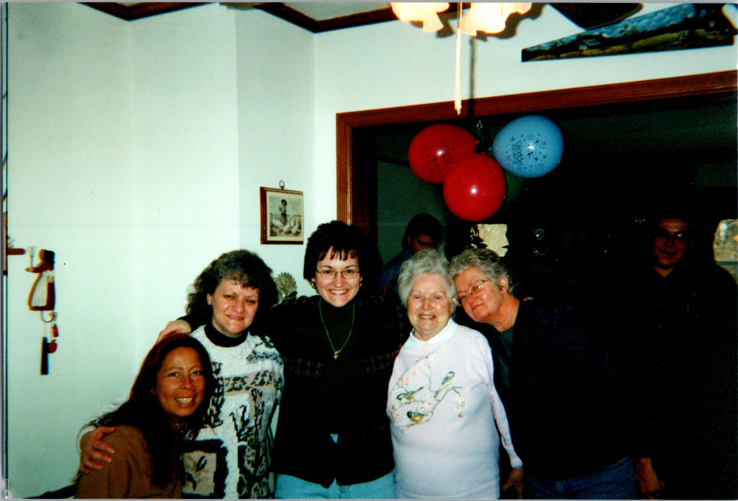 Group of smiling women posing together at a party indoors, with red and blue balloons in the background.