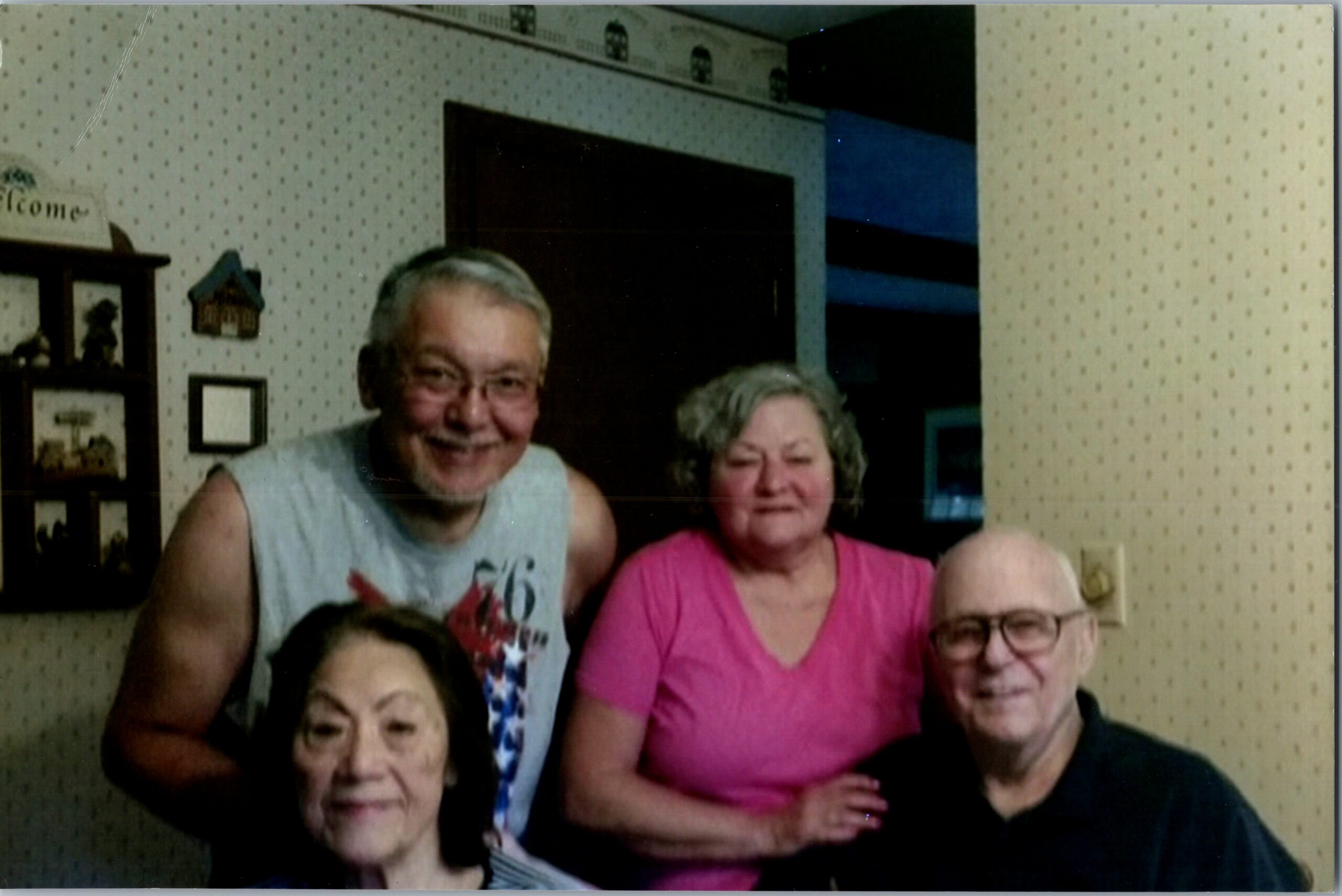 A smiling family group posing indoors against patterned wallpaper in a home, closely gathered for a photo.
