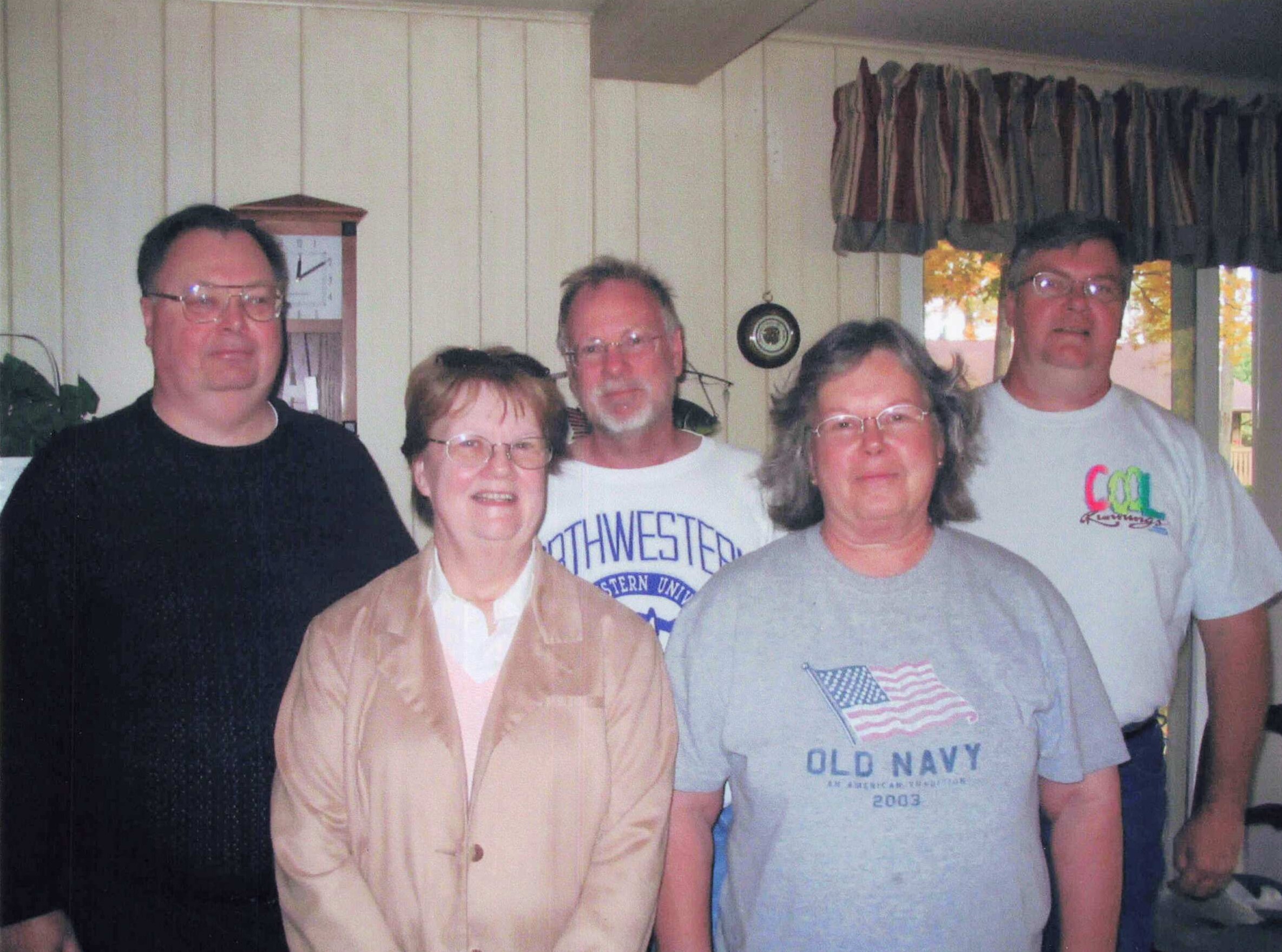 Group of five adults posing together indoors for a casual photo.