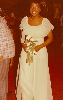Woman in a light-colored off-shoulder dress holding a bouquet of white flowers at a formal event on a red carpet.