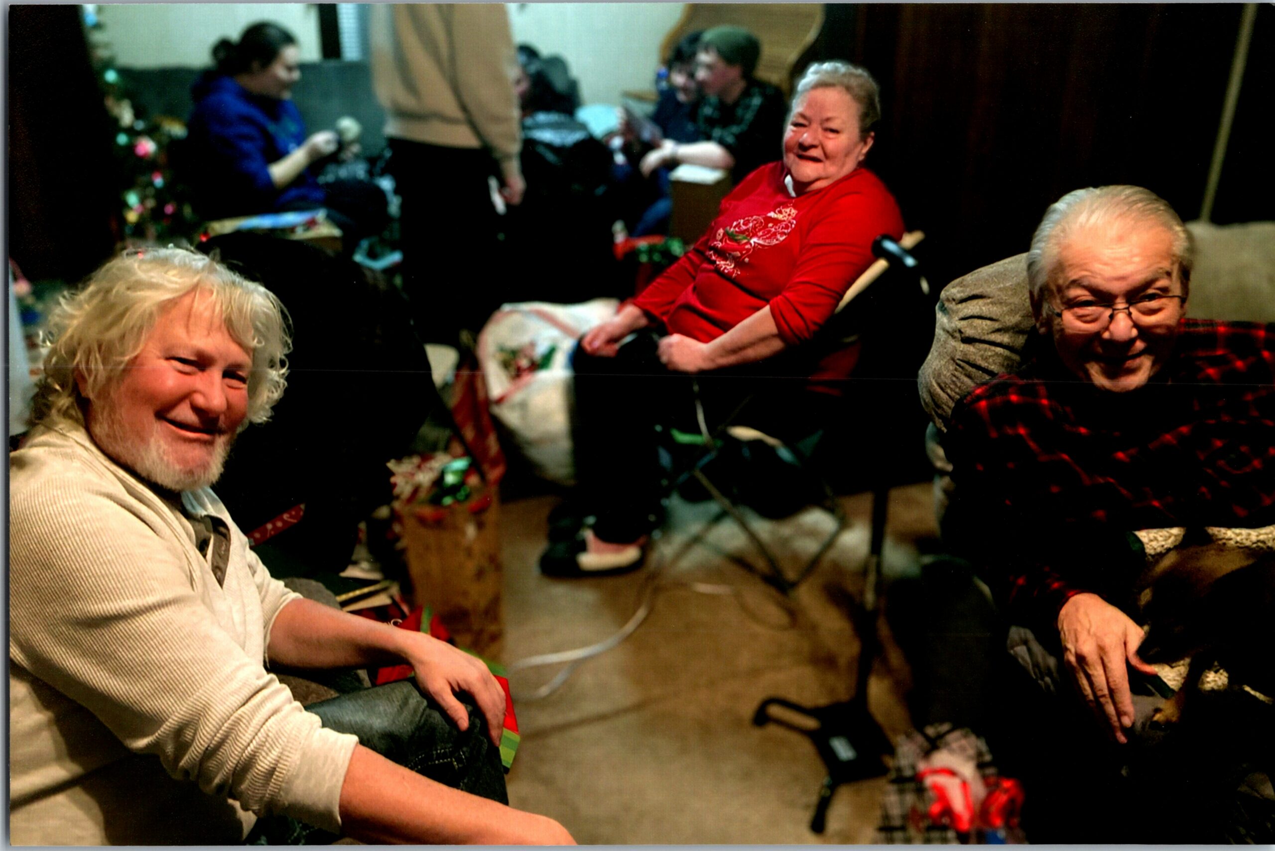 Smiling seniors seated in a cozy room during a holiday gathering, with gifts and a Christmas tree in the background
