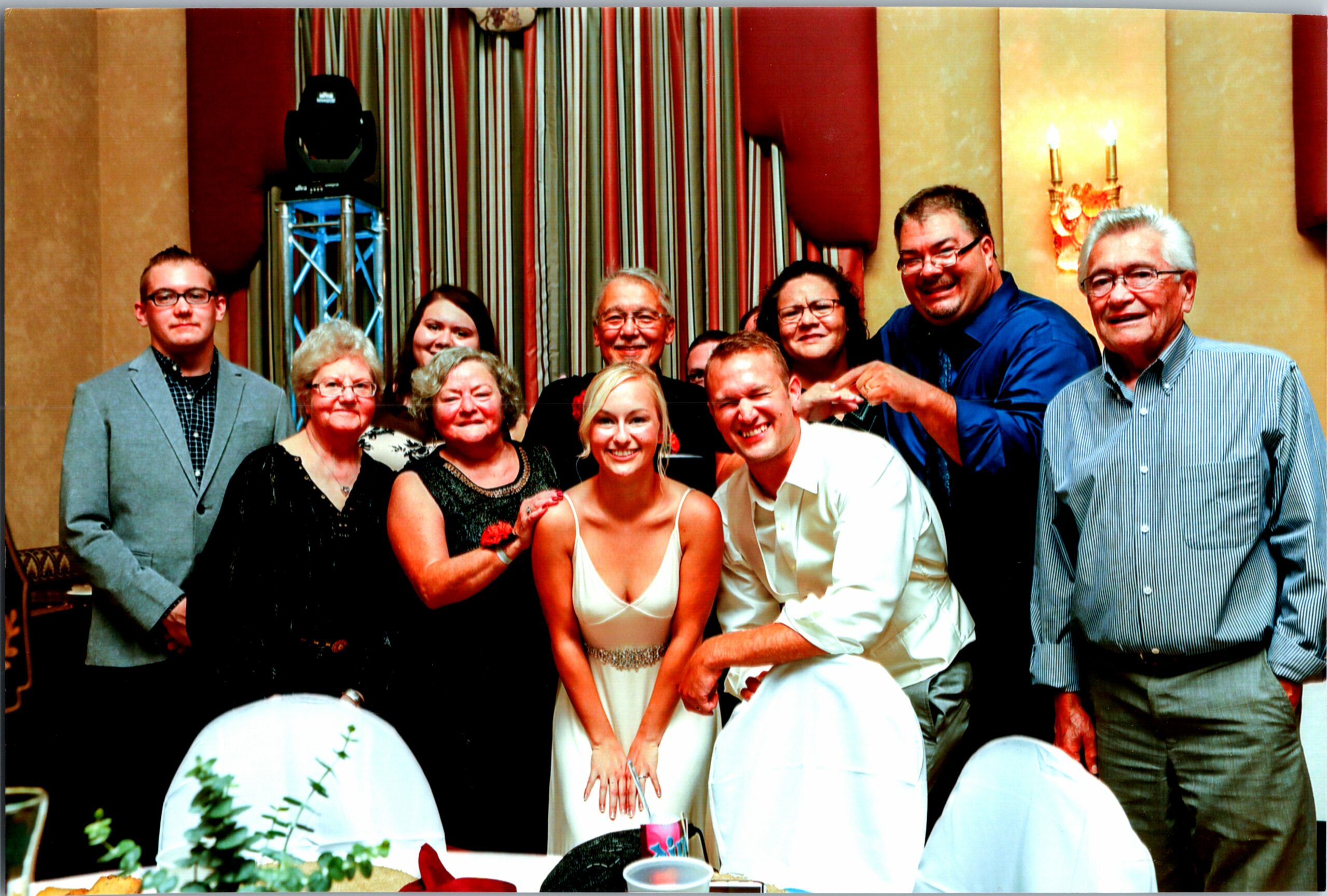 Group of smiling guests at a wedding reception posing for a photo around a table in formal attire.