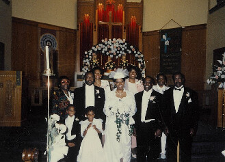 Bride and groom pose with their wedding party in a church sanctuary, flanked by friends and family on both sides.