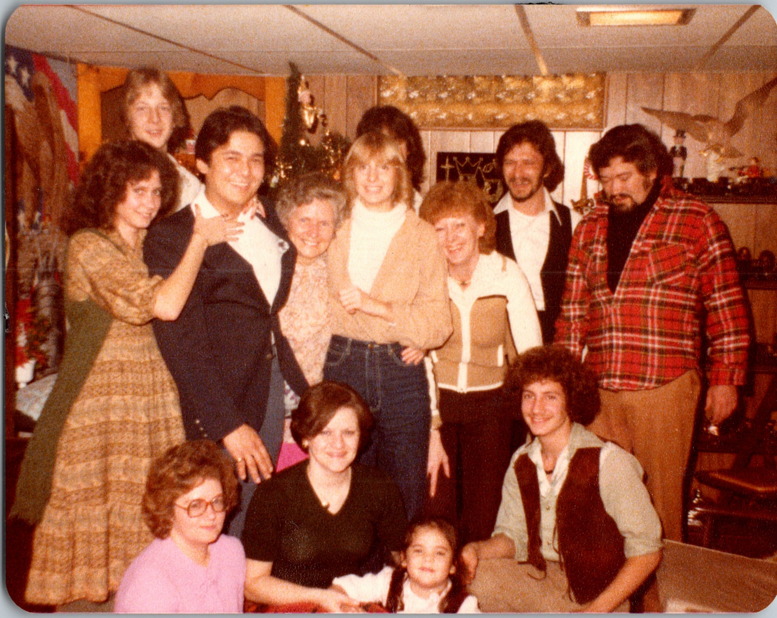 Group of friends and family posing for a 1970s-style photo at a party in a wood-paneled room. (informative)