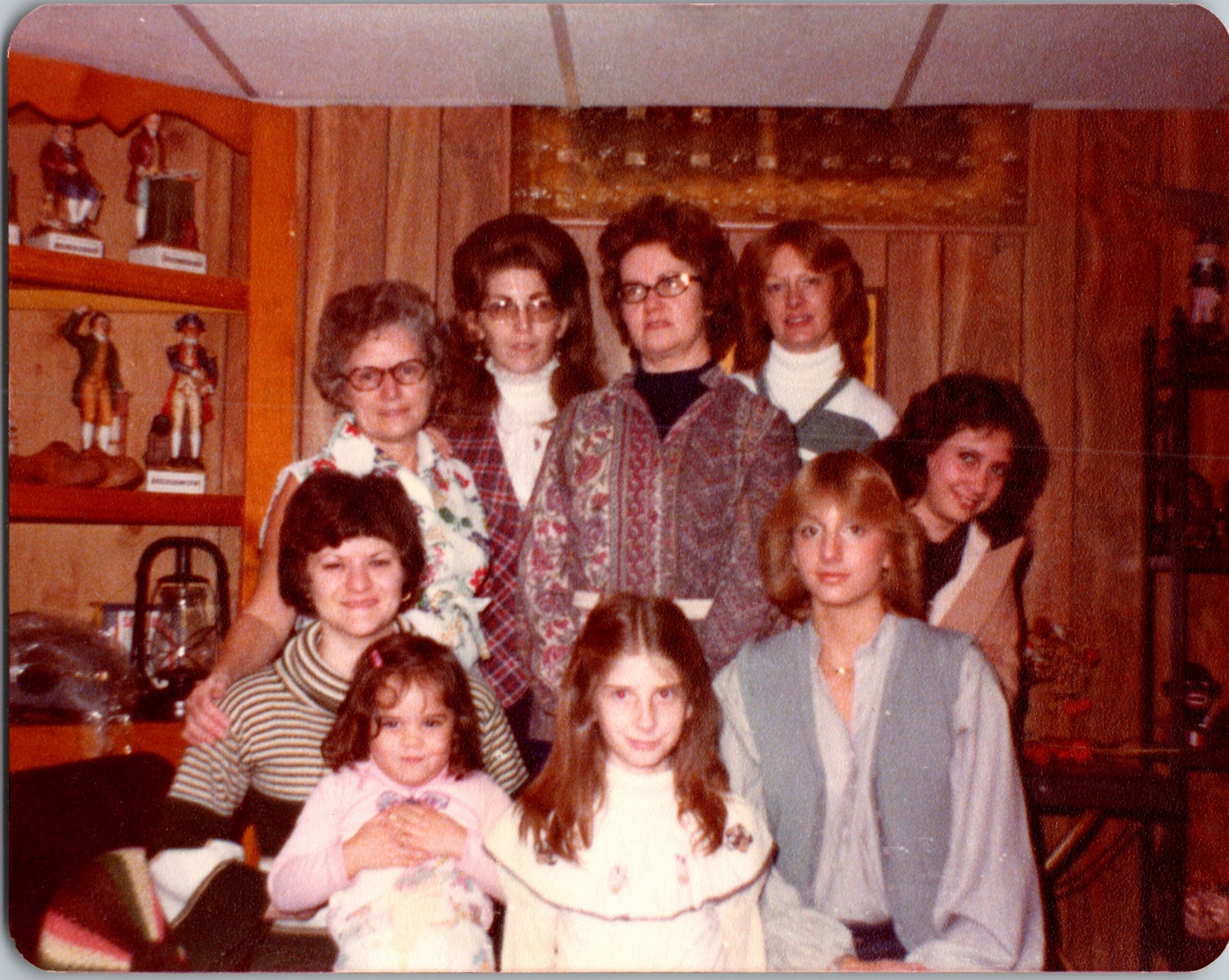 Group of people posing for a family photo in a living room with wooden shelves and decorative figurines in the background.