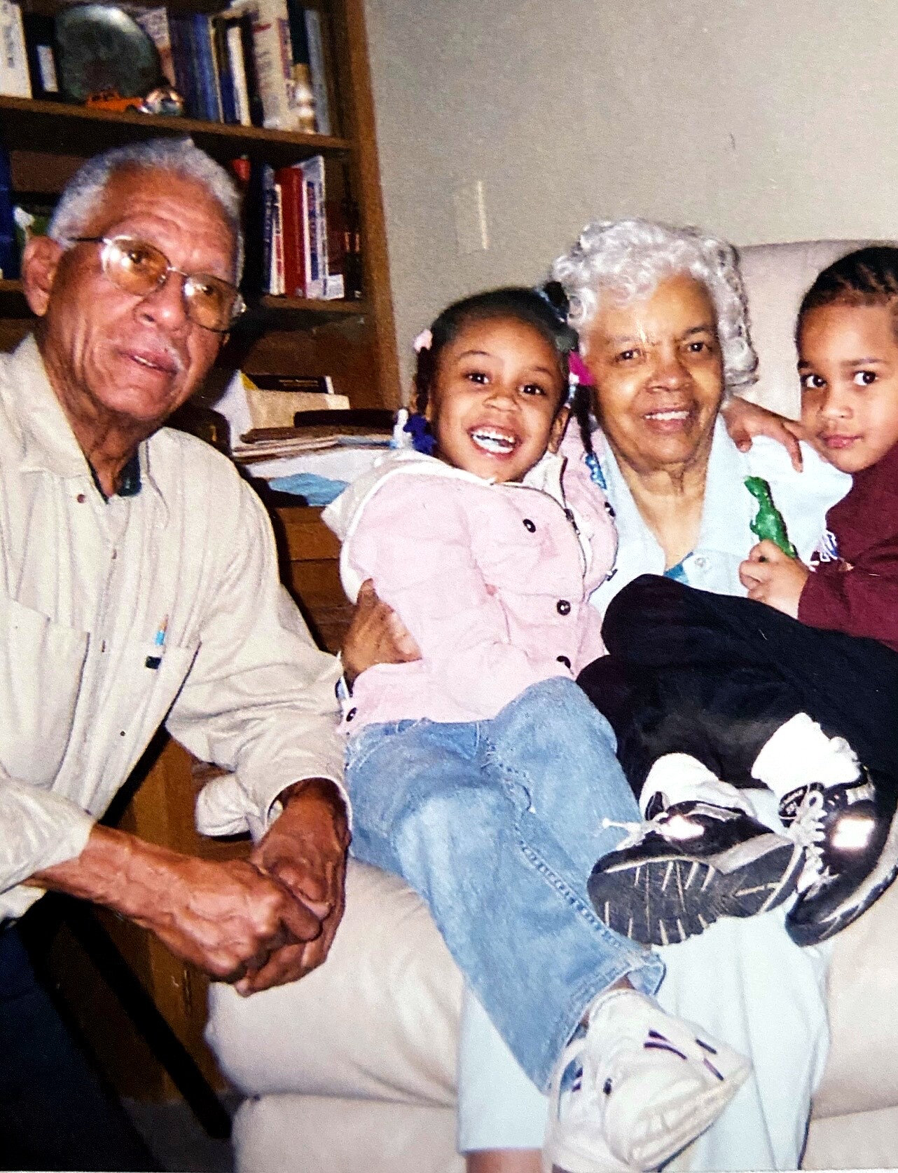 Elderly couple seated with two children on a couch, all smiling at the camera in a living room setting.