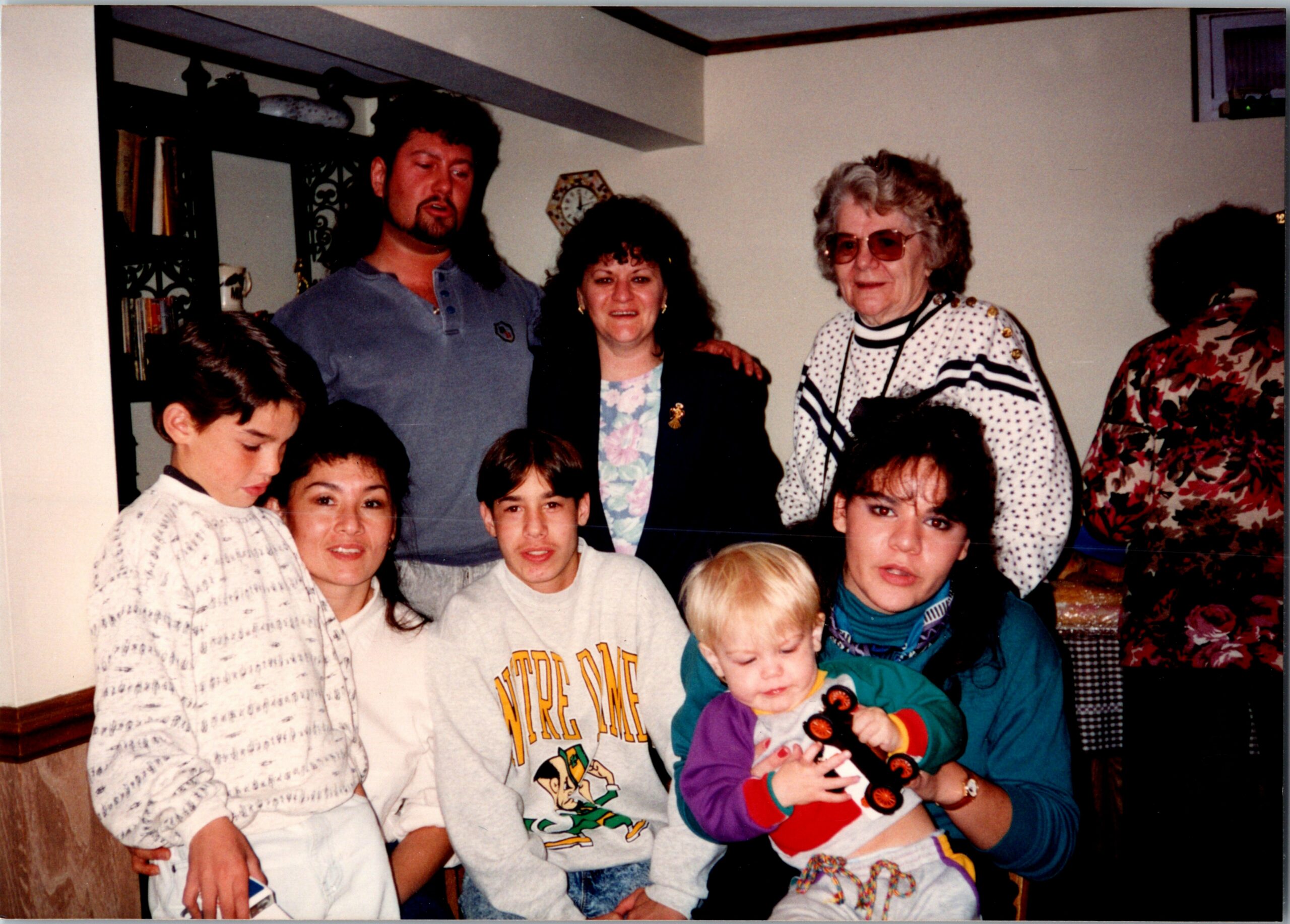 Family group posing for a photo indoors in a living room, with adults in back and several children, including a baby, in front.