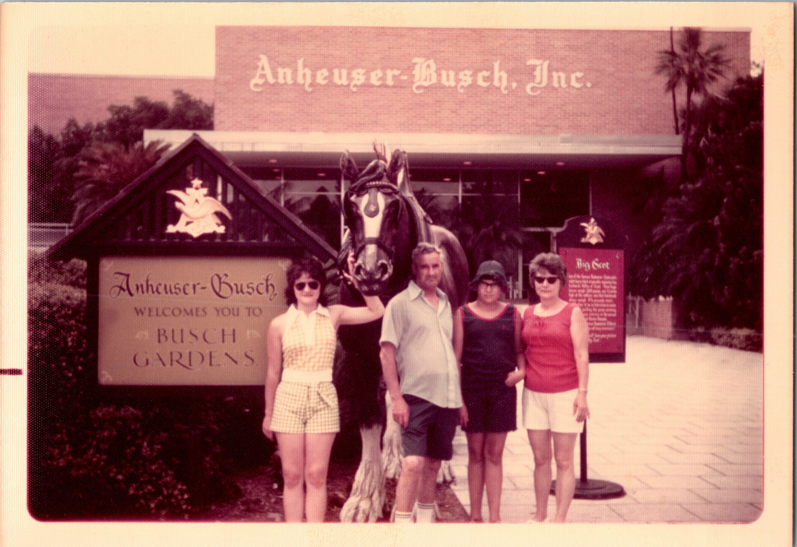 Five people pose in front of the Anheuser-Busch Gardens entrance, with a decorative horse statue between them.