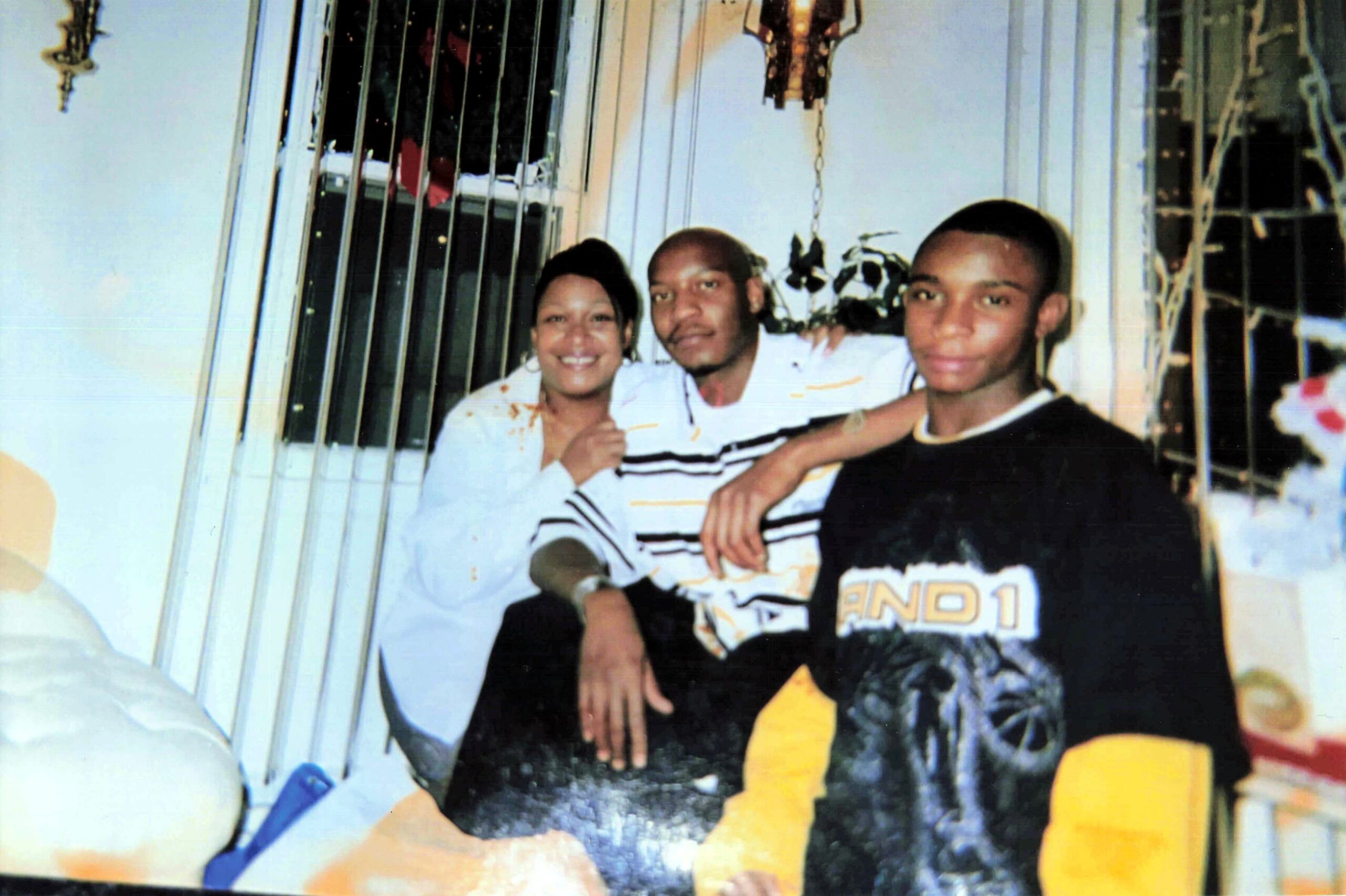 Three friends posing indoors for a casual photo: a smiling woman on the left, a man in a striped shirt in the center, and a young man in a black shirt on the right.